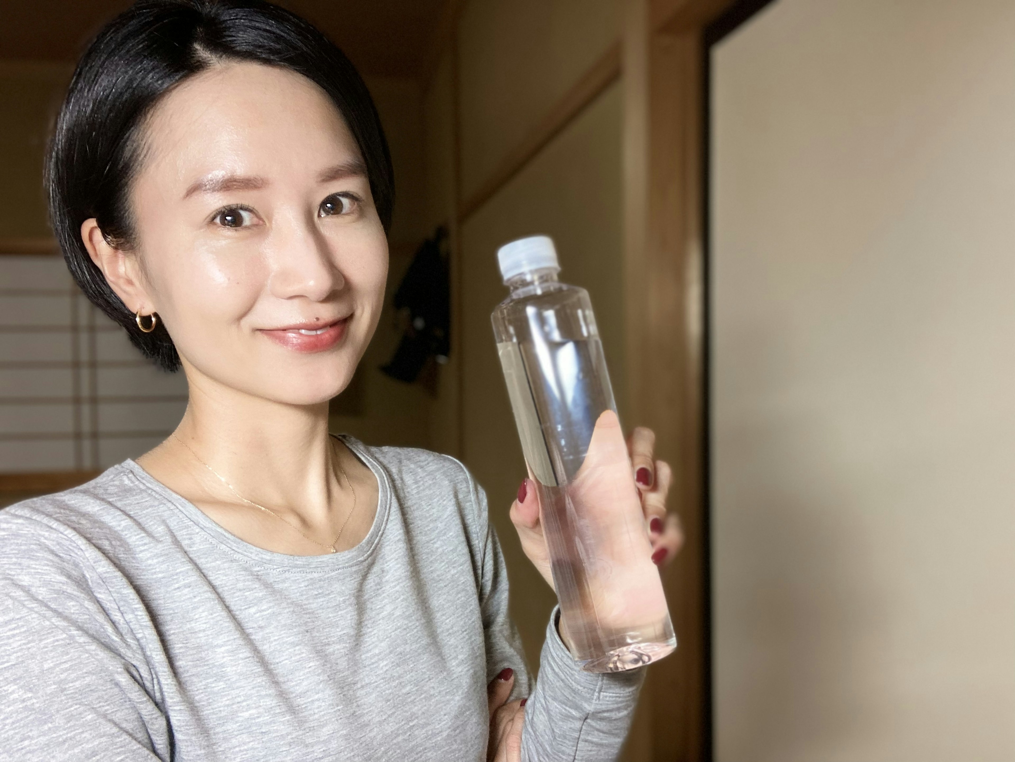 Una donna sorridente che tiene una bottiglia d'acqua trasparente in un ambiente interno