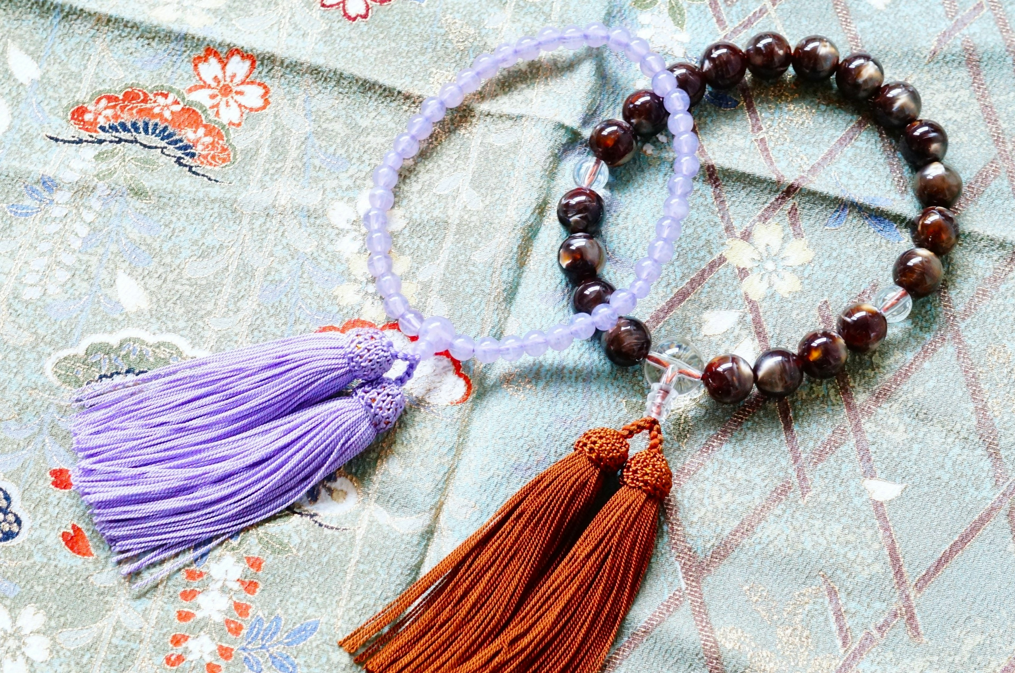 Deux bracelets avec des pompons violets et marron exposés sur un tissu décoratif