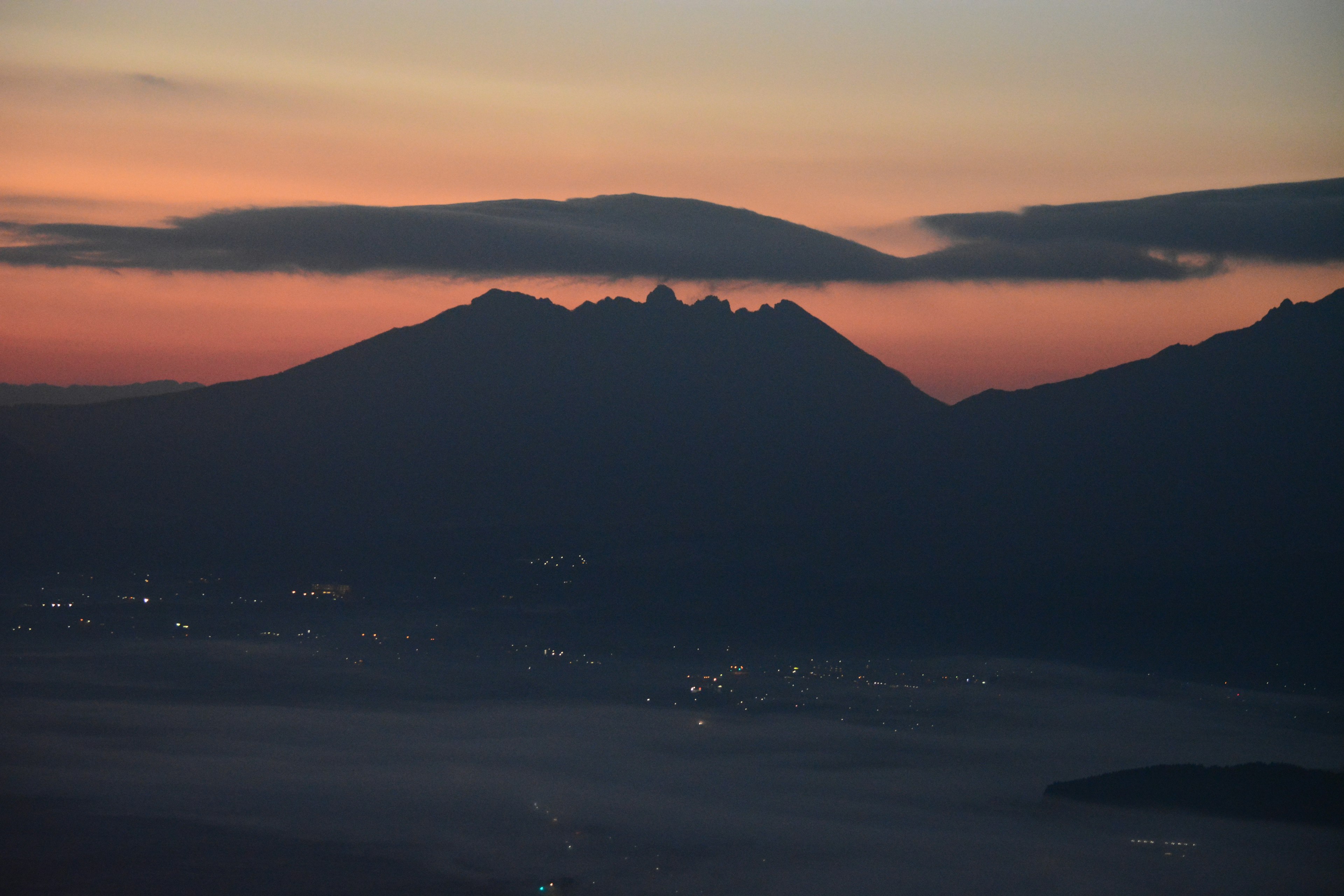 夕焼けの中に浮かぶ山のシルエットと街の明かり