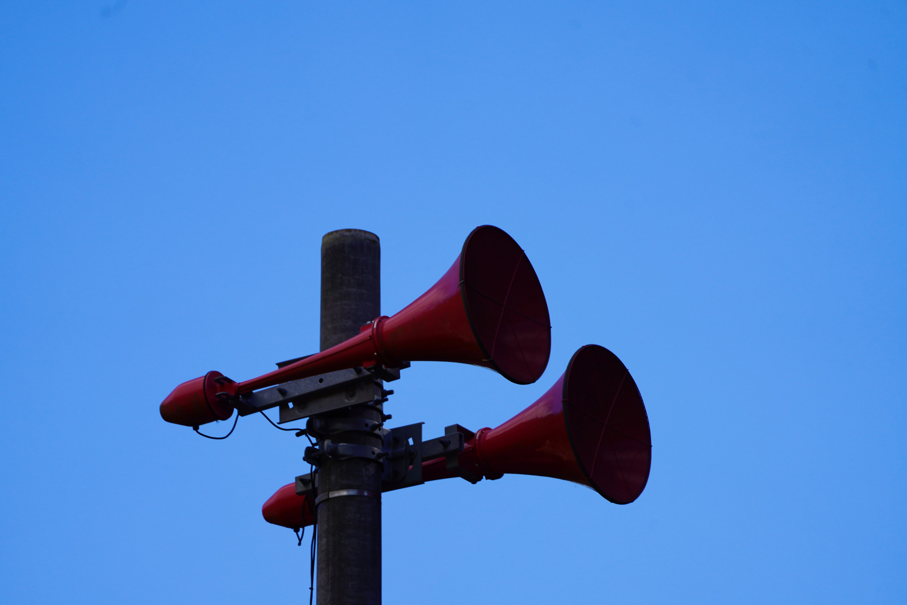 Altavoces en forma de cuerno rojos montados en un poste contra un cielo azul