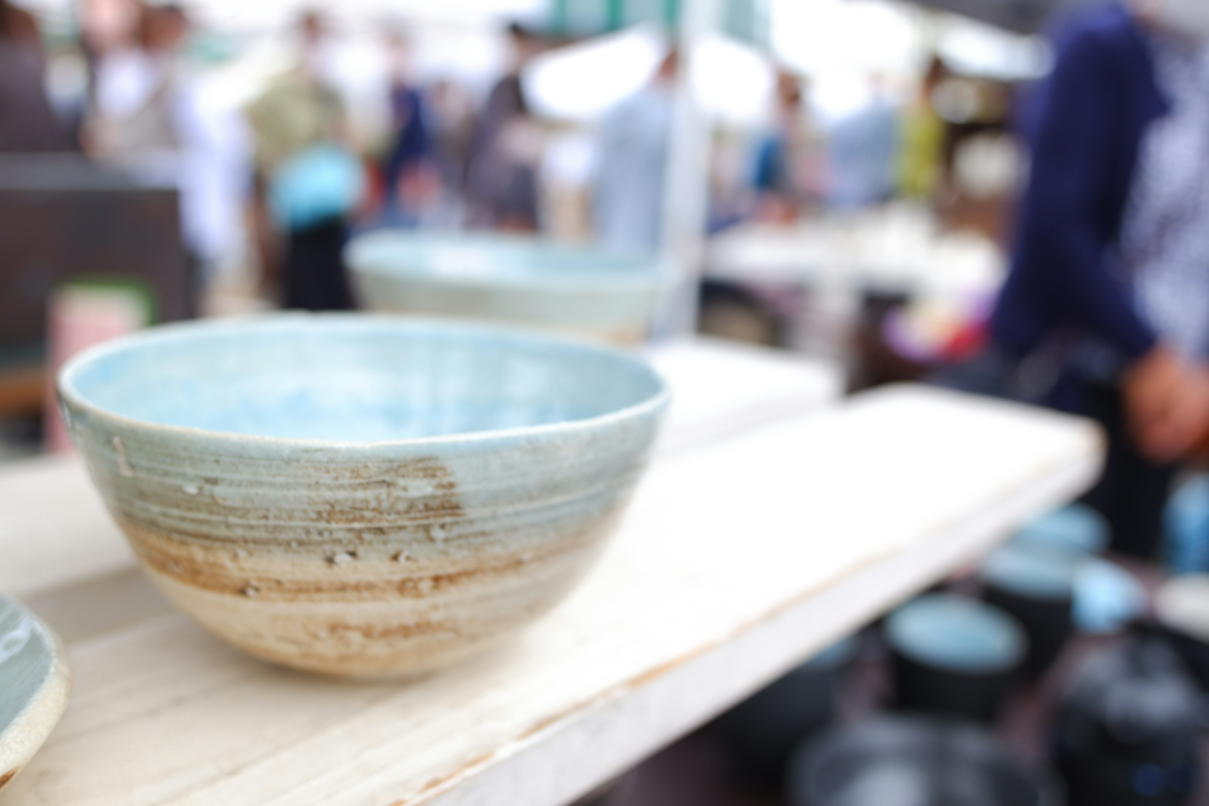 Ceramic bowl with blue glaze displayed on wooden shelf at a pottery market