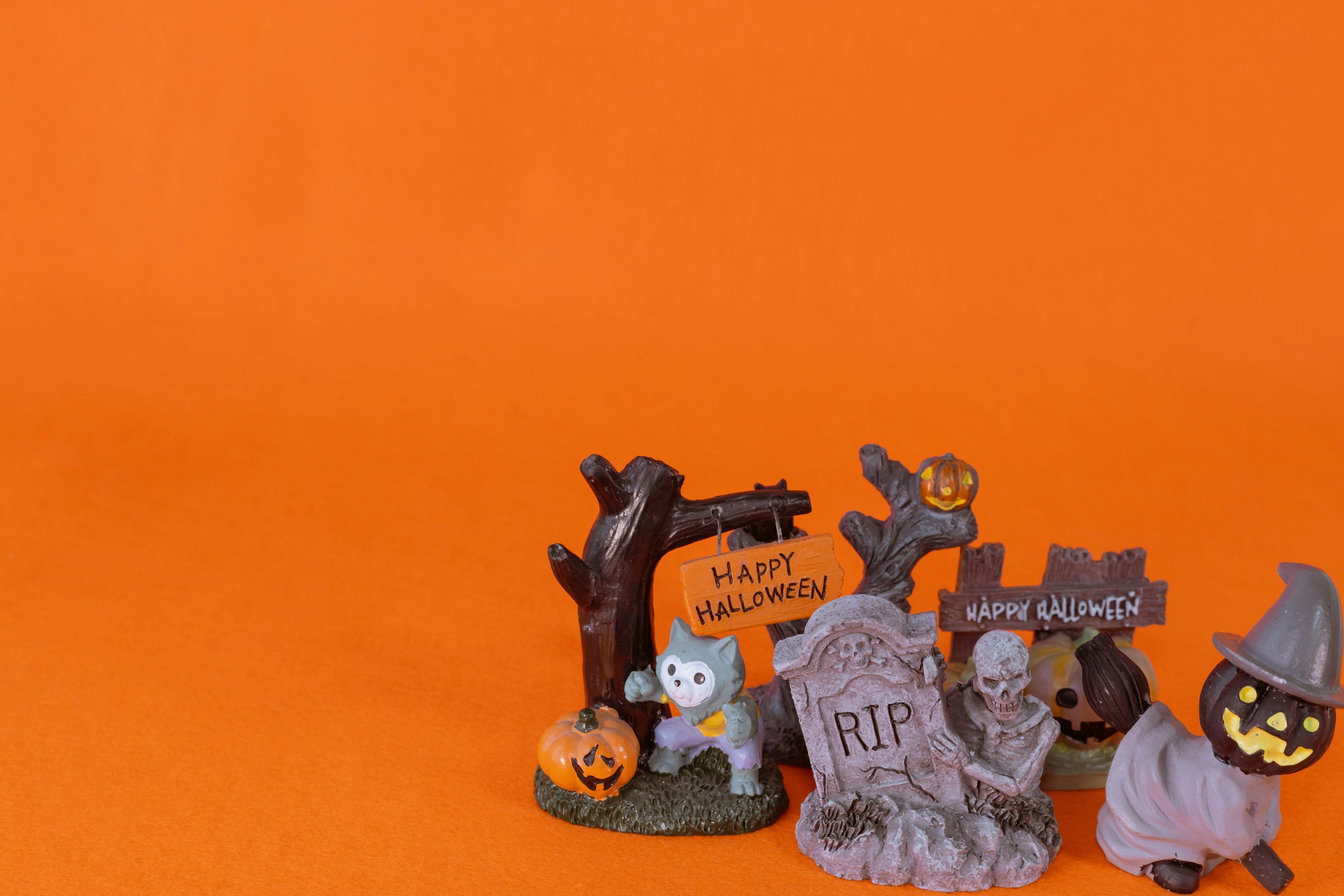 Halloween decorations featuring a ghost, gravestones, pumpkins, and a witch against an orange background