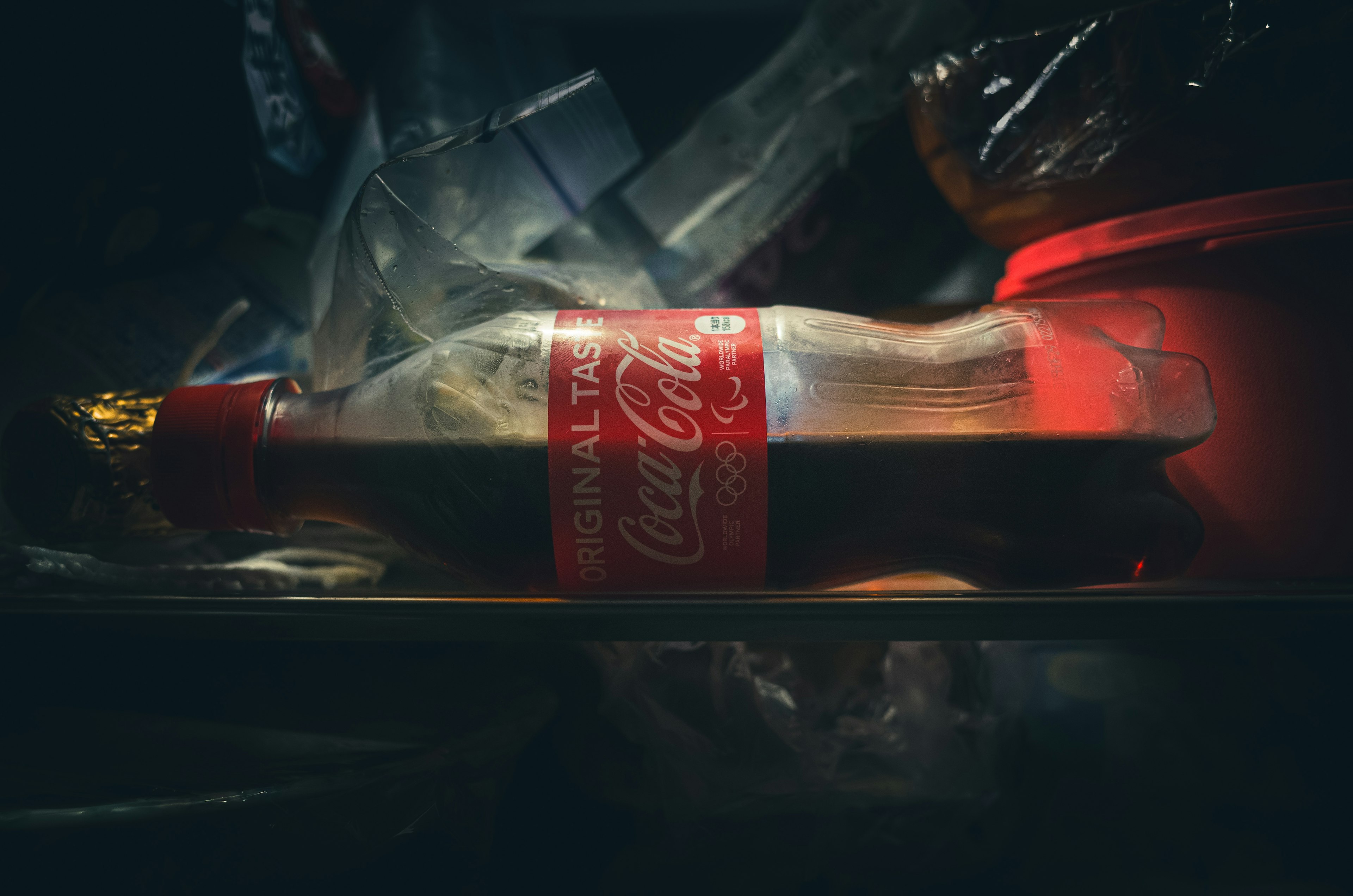 Coca-Cola-Flasche in einem Kühlschrank umgeben von Plastikverpackungen