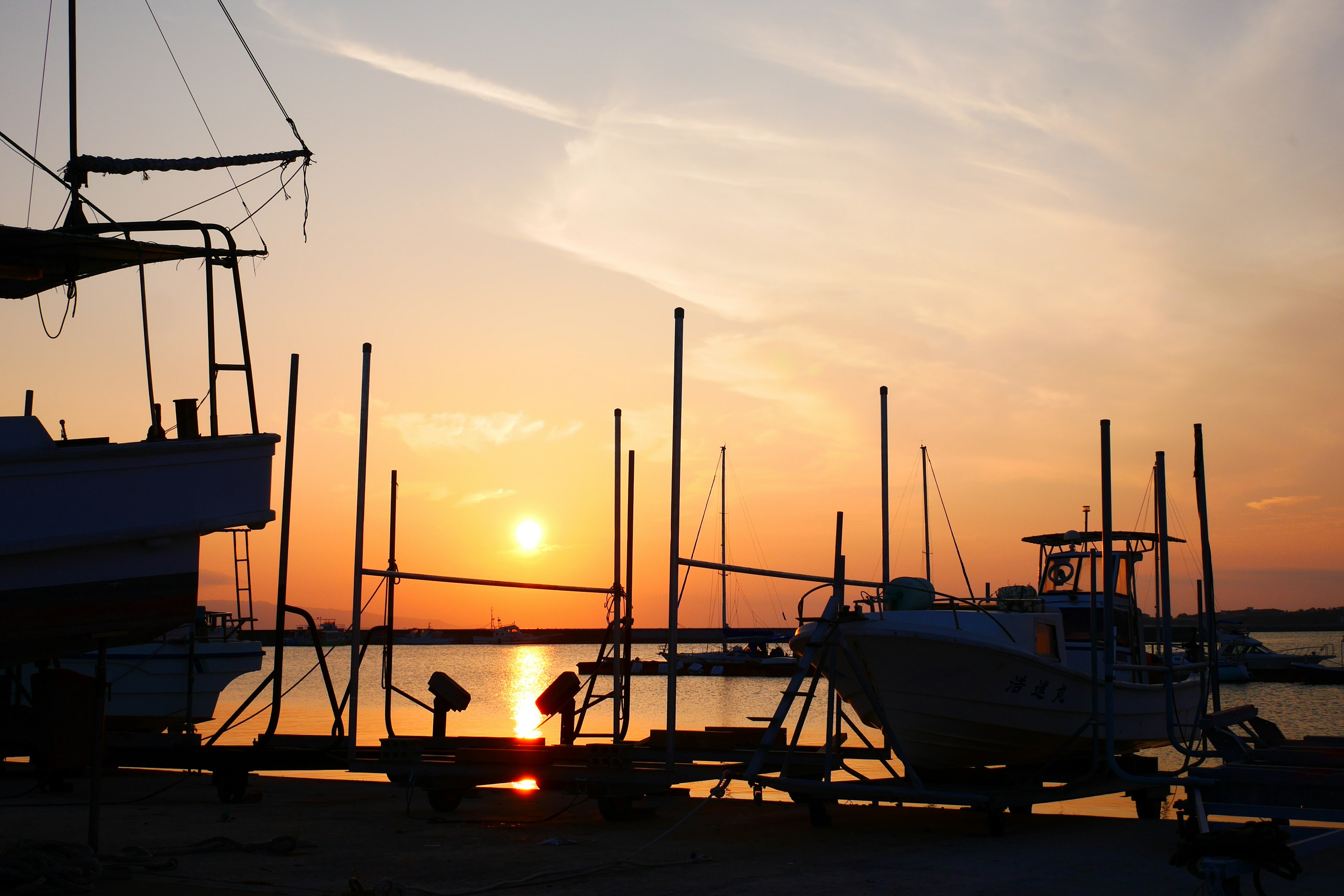 Boats docked at a harbor during sunset with masts silhouetted