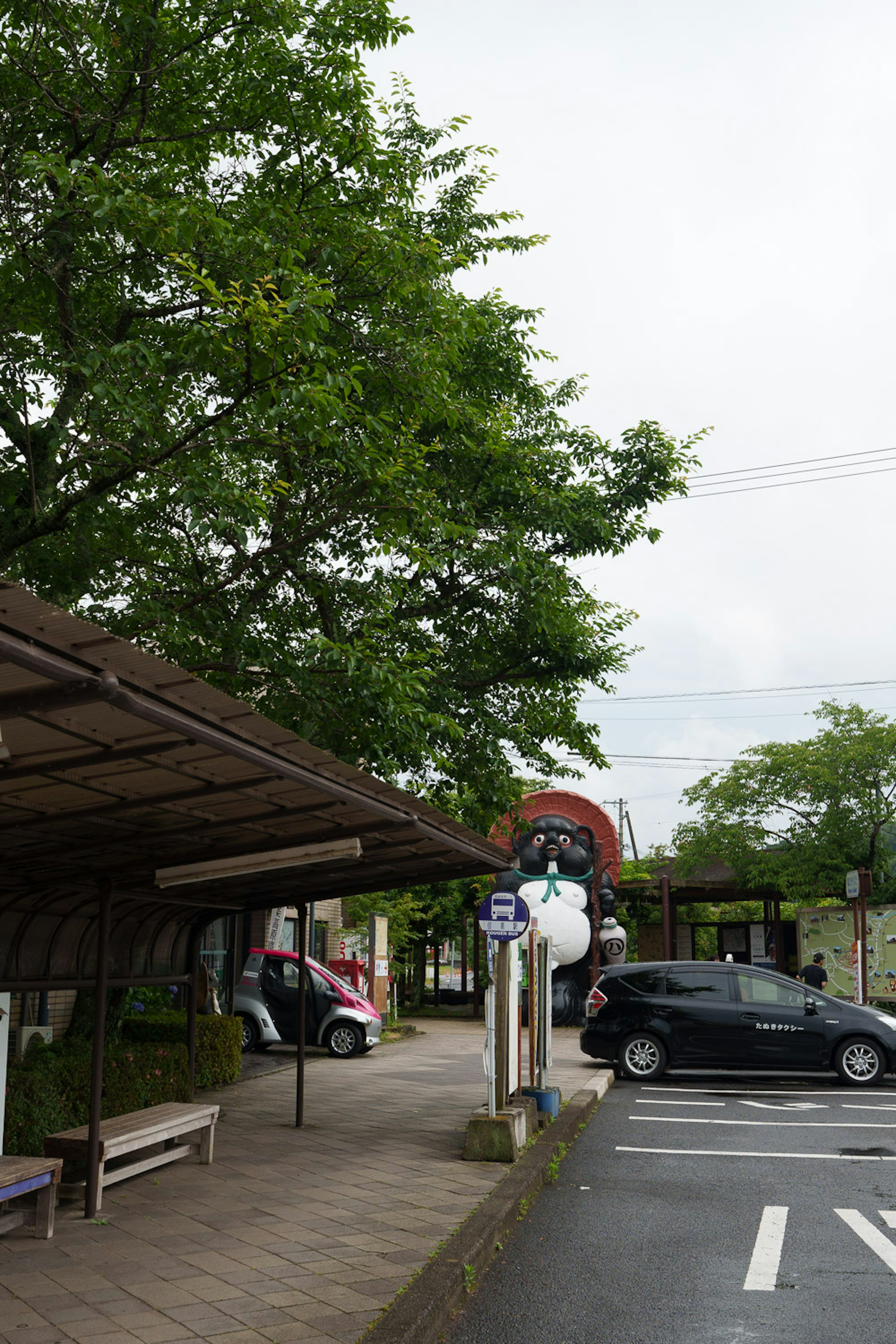 Scenic view of a bus stop with green trees and parked cars