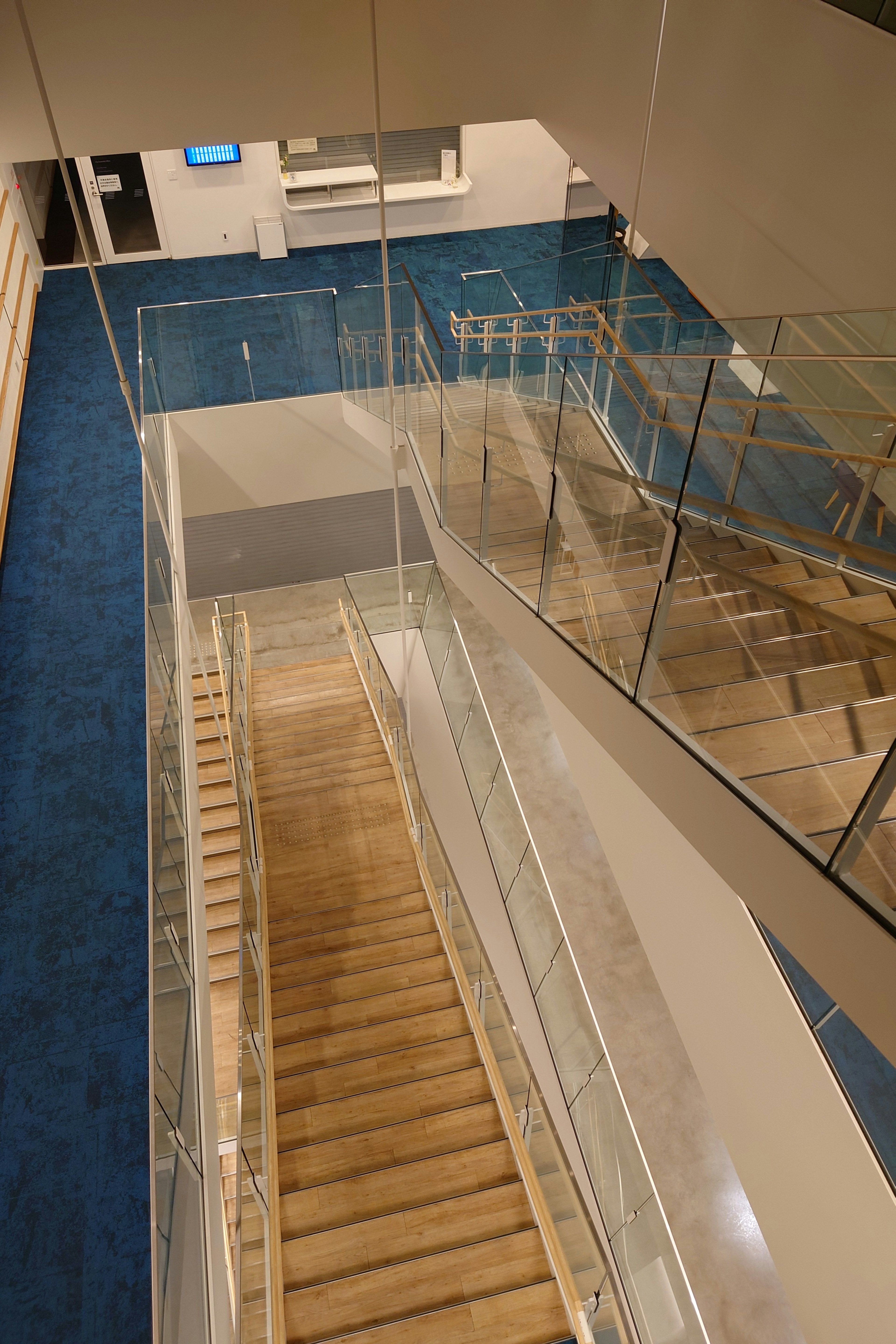 Escalier intérieur moderne avec des marches en bois et une rampe en verre vu d'en haut