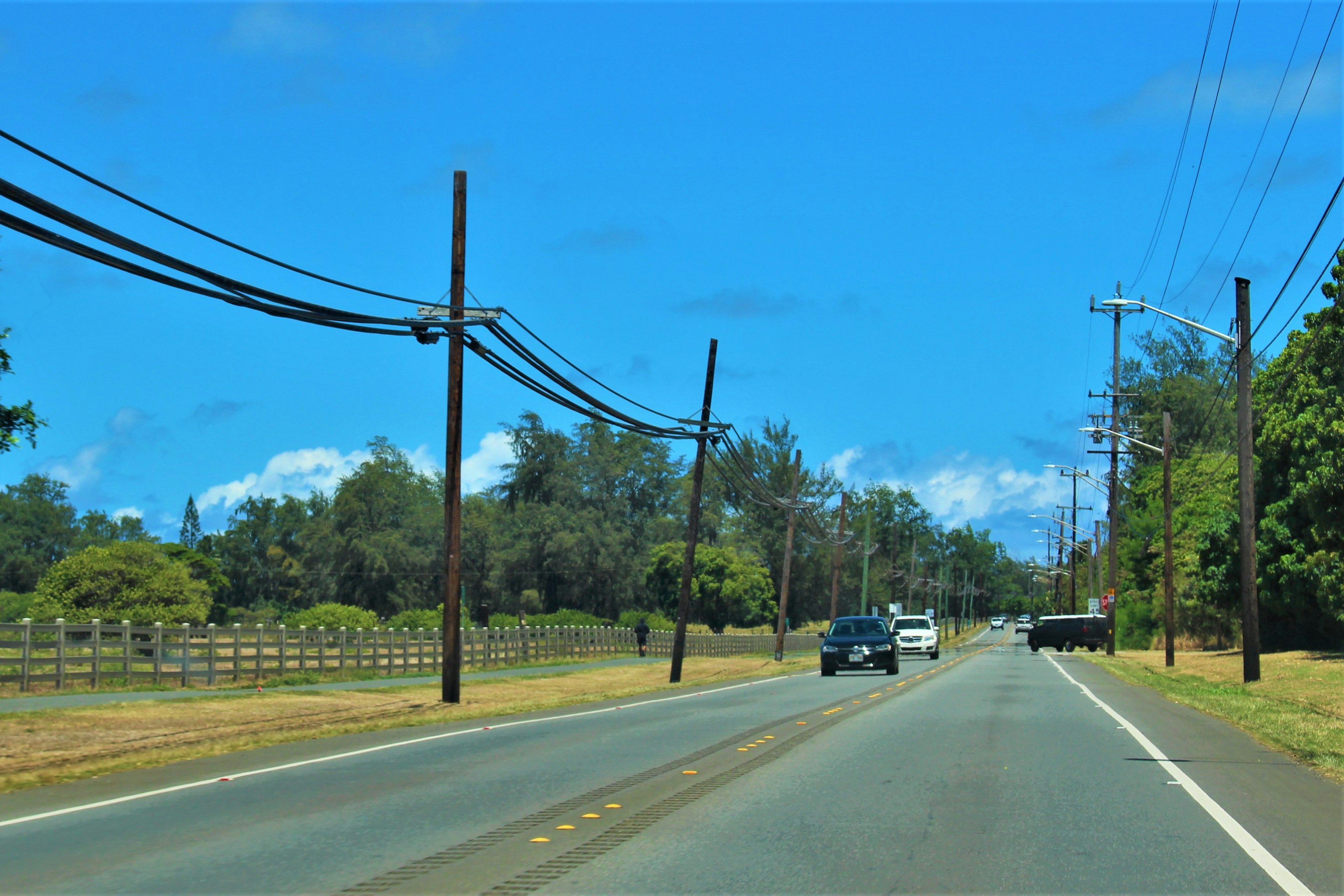 Escena de carretera rural con postes de electricidad y coches bajo un cielo azul