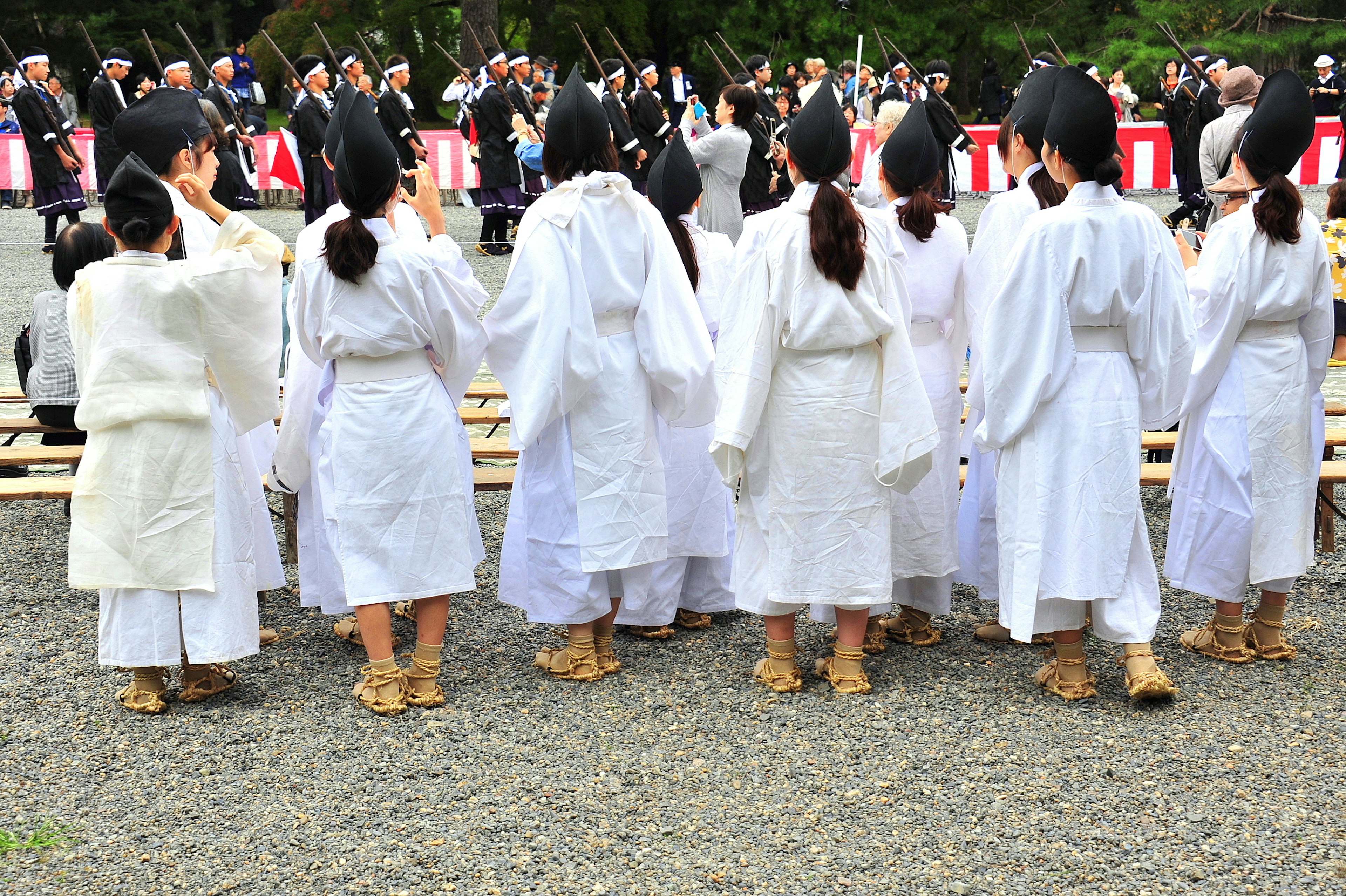 白い衣装を着た女性たちが後ろ向きに立っている神社の祭りの風景