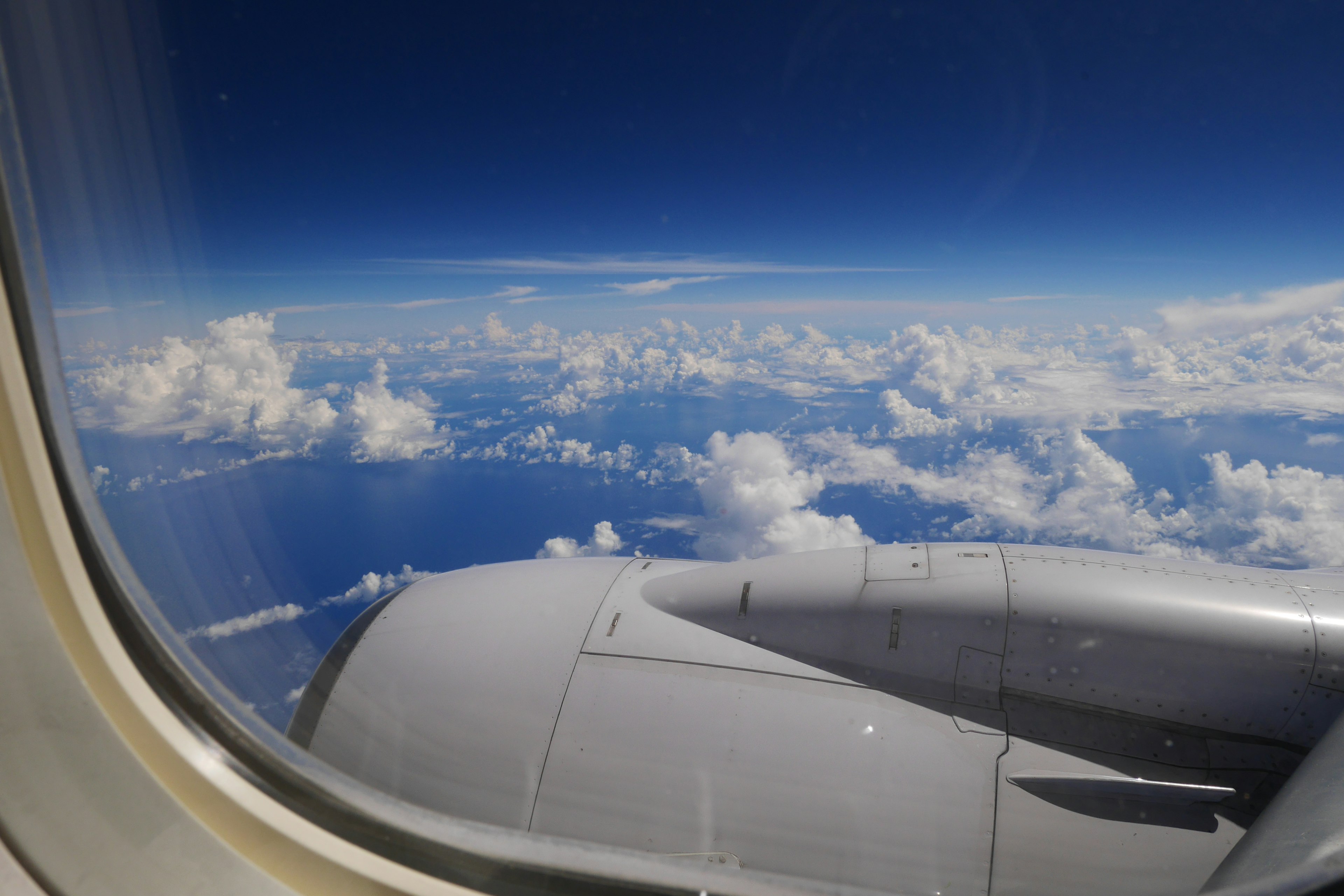 View from an airplane window showing blue sky and clouds with a part of the engine visible