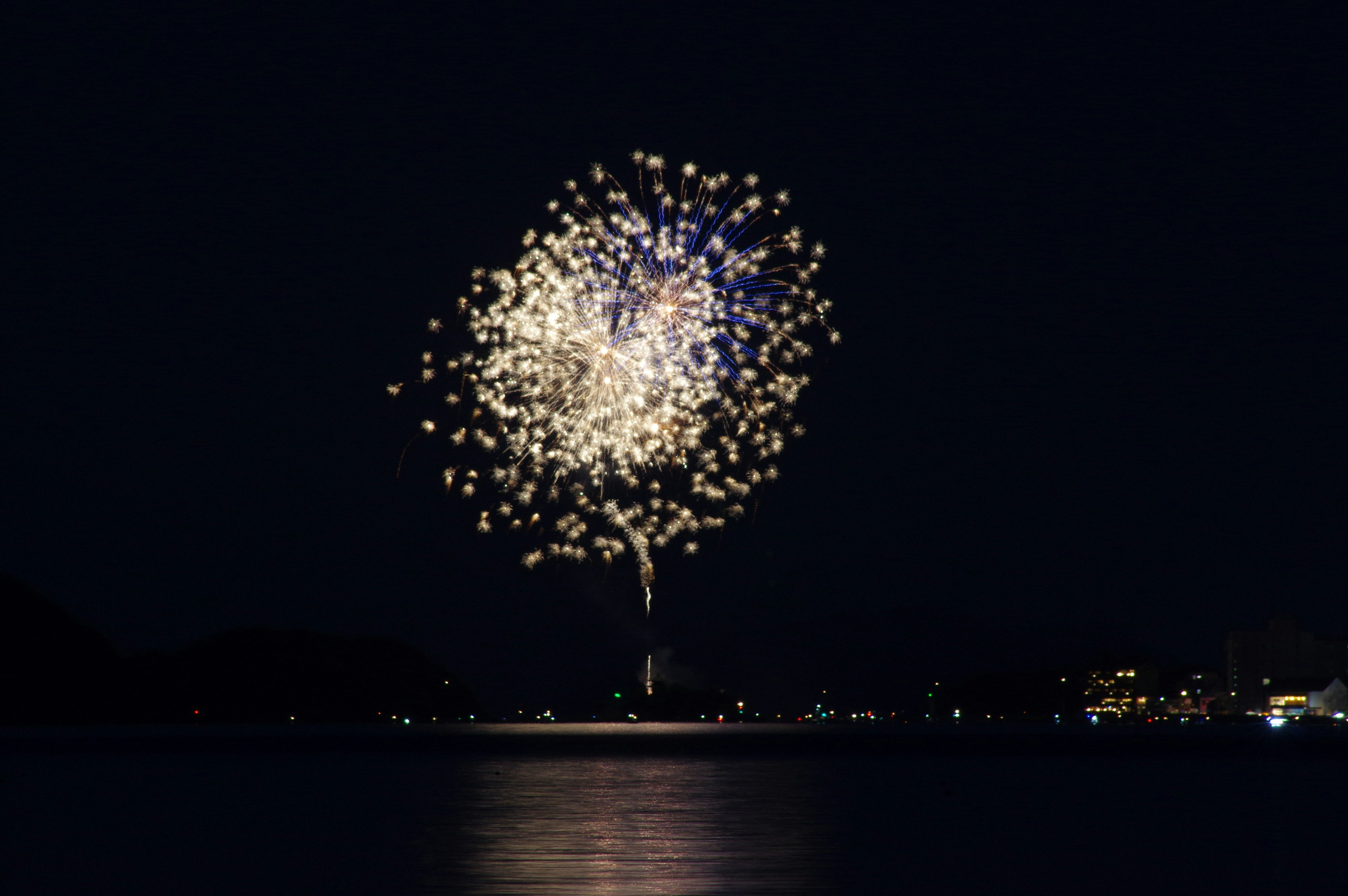 Un gran estallido de fuegos artificiales iluminando el cielo nocturno reflejado en el agua