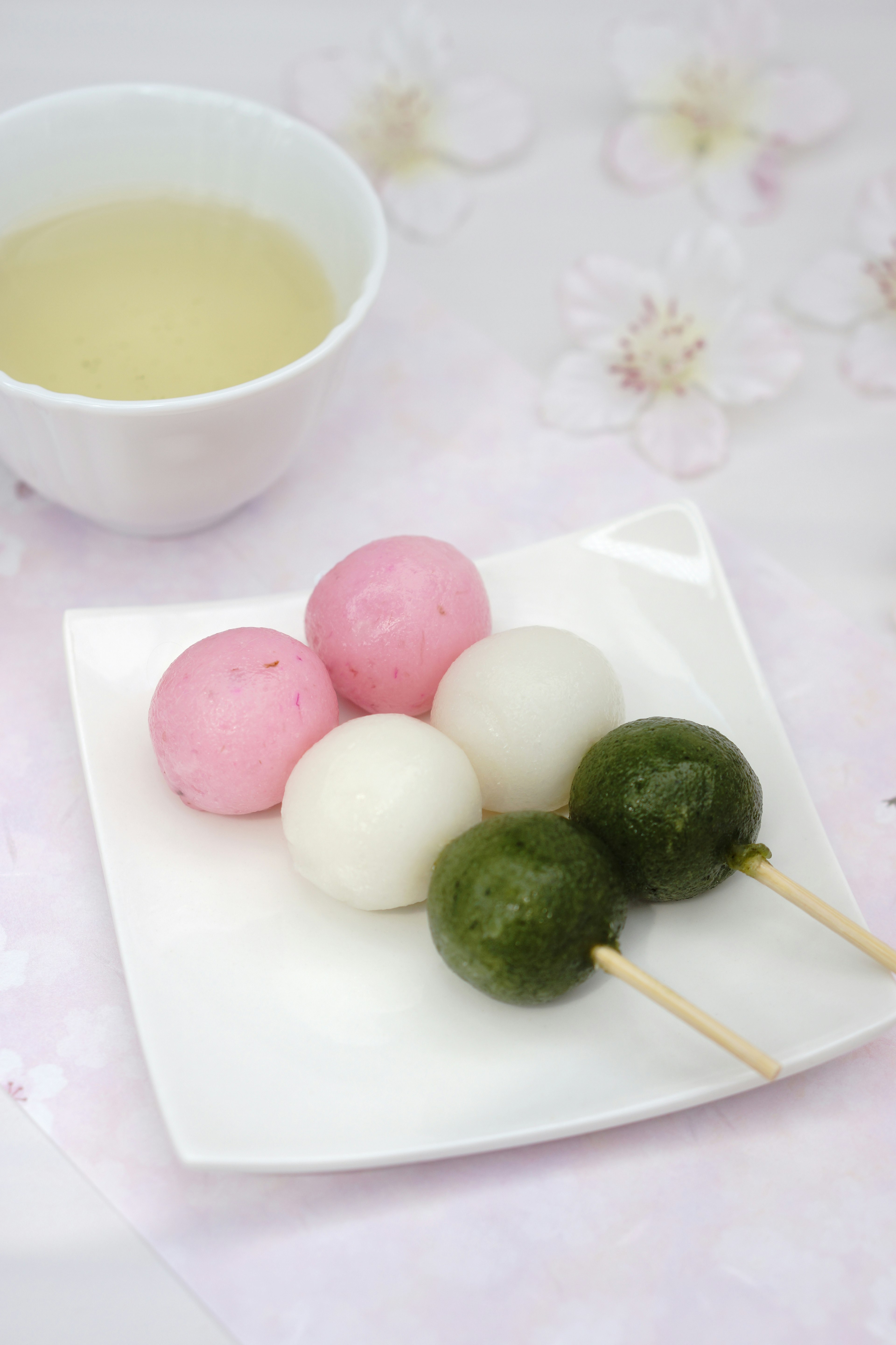 Dango berwarna-warni disusun di atas piring putih dengan secangkir teh di samping