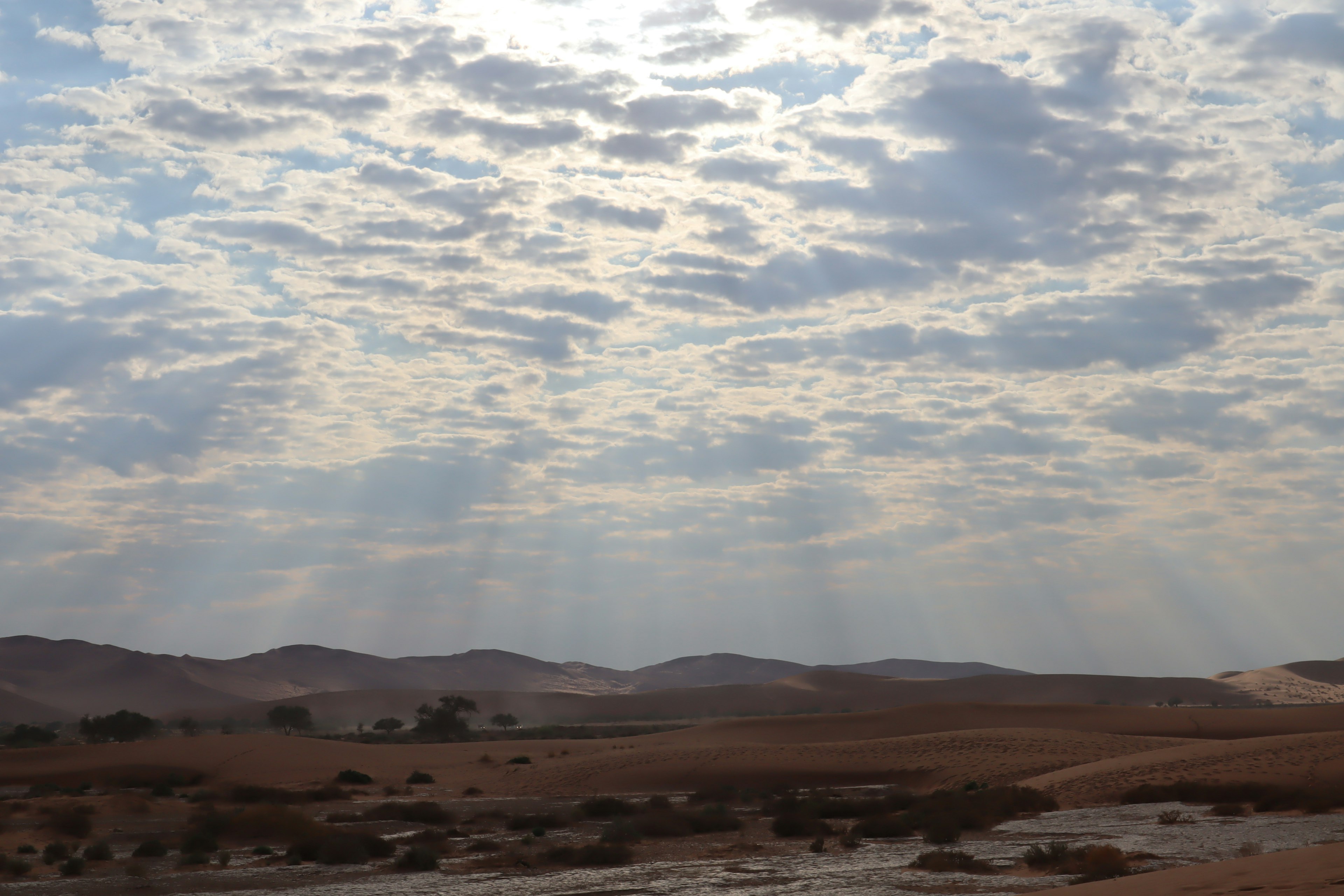 Dunes de sable expansives sous un ciel nuageux avec des rayons de lumière