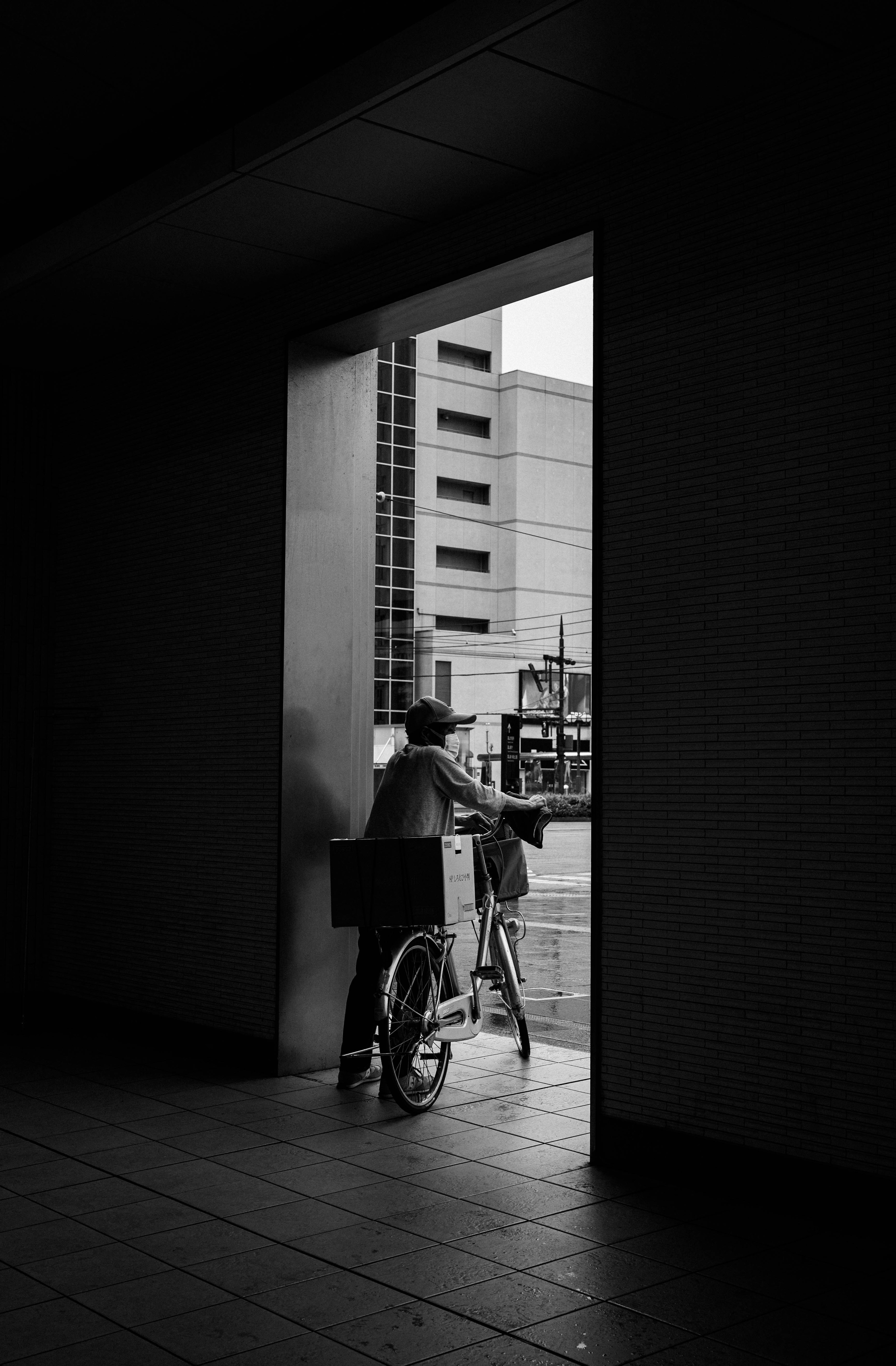 Ein Lieferant auf einem Fahrrad, der durch eine offene Tür in einem Schwarzweißfoto schaut