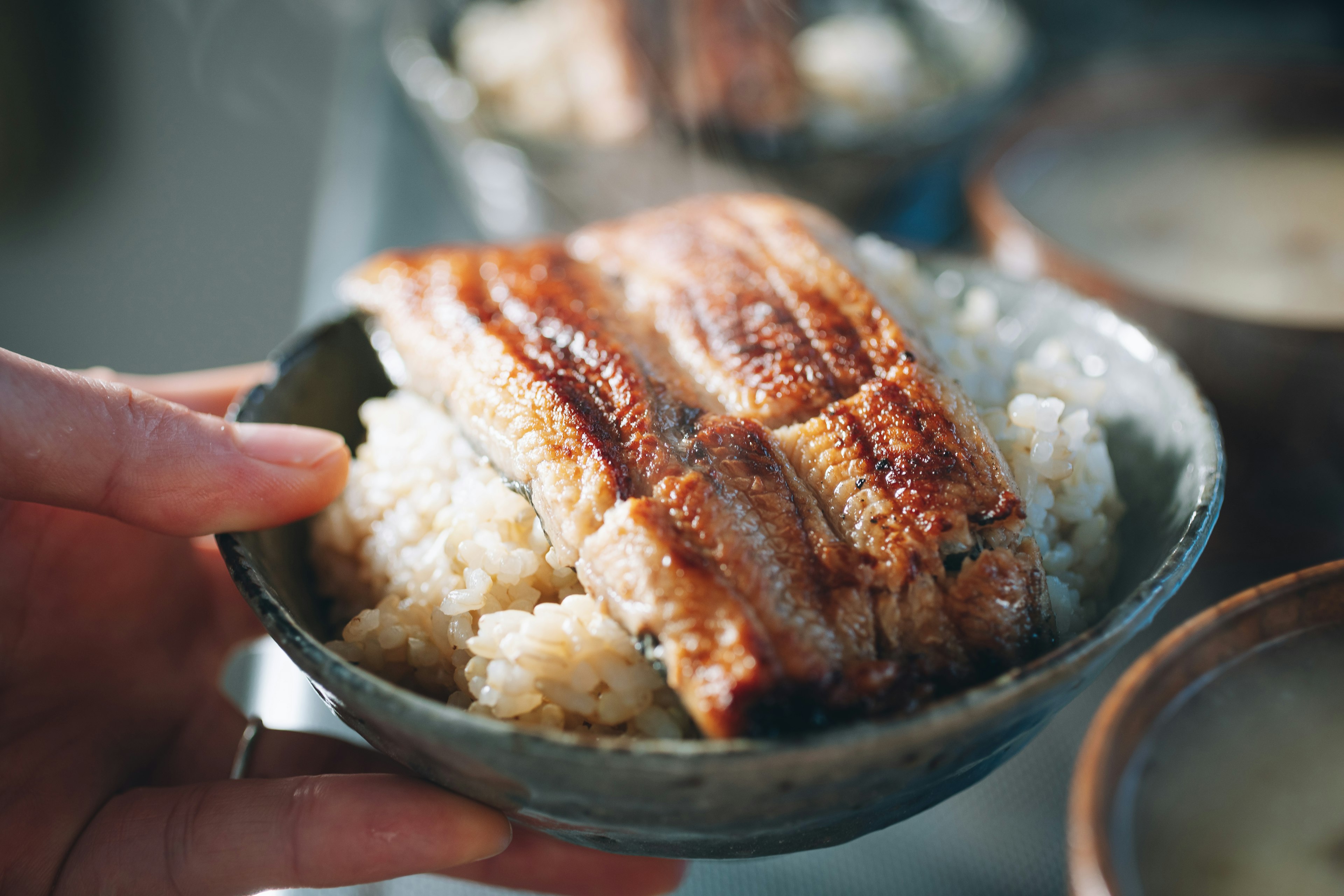 焼きウナギとご飯を盛った器を持つ手