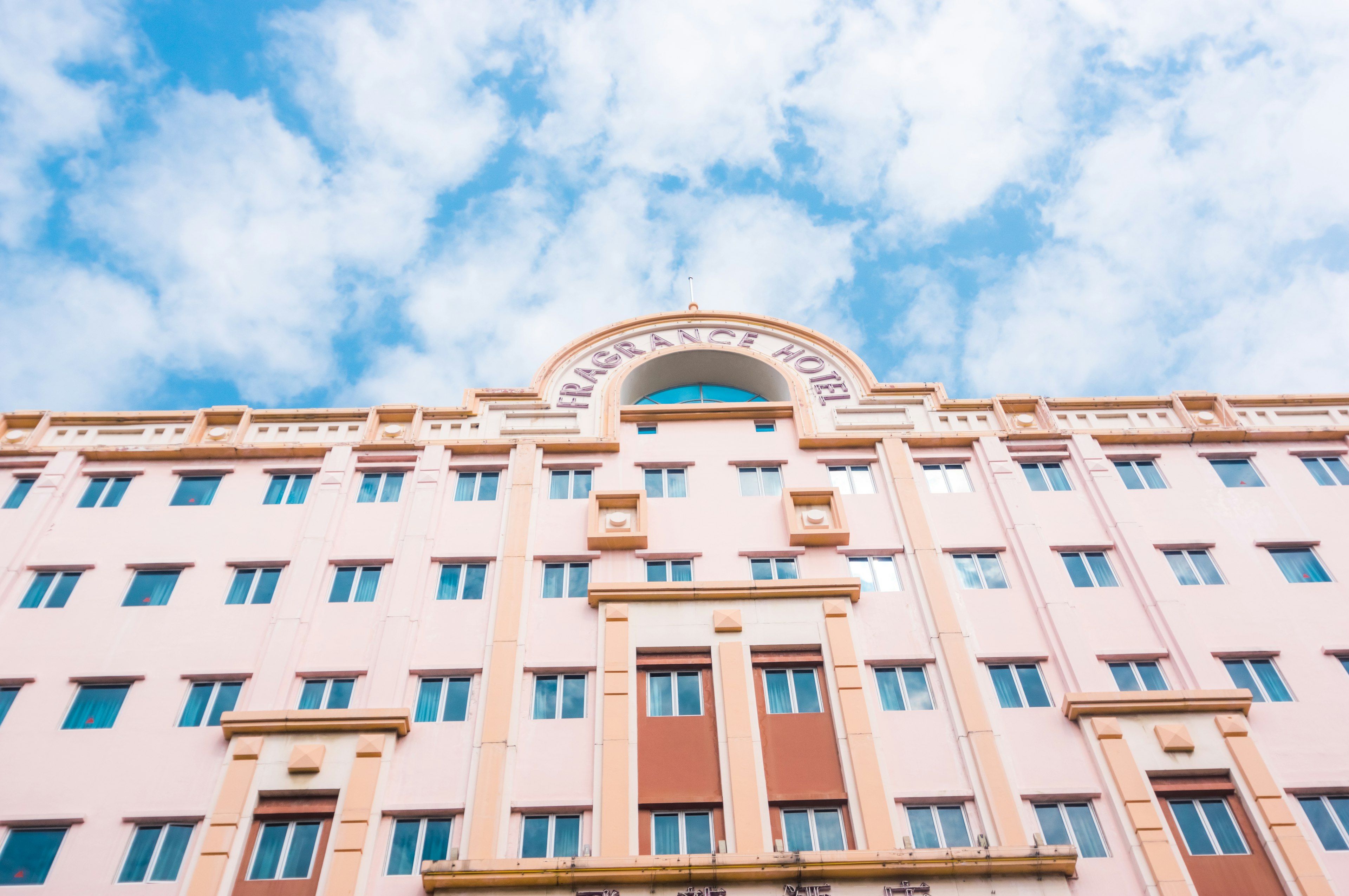 Fachada de un edificio rosa bajo un cielo azul con nubes blancas