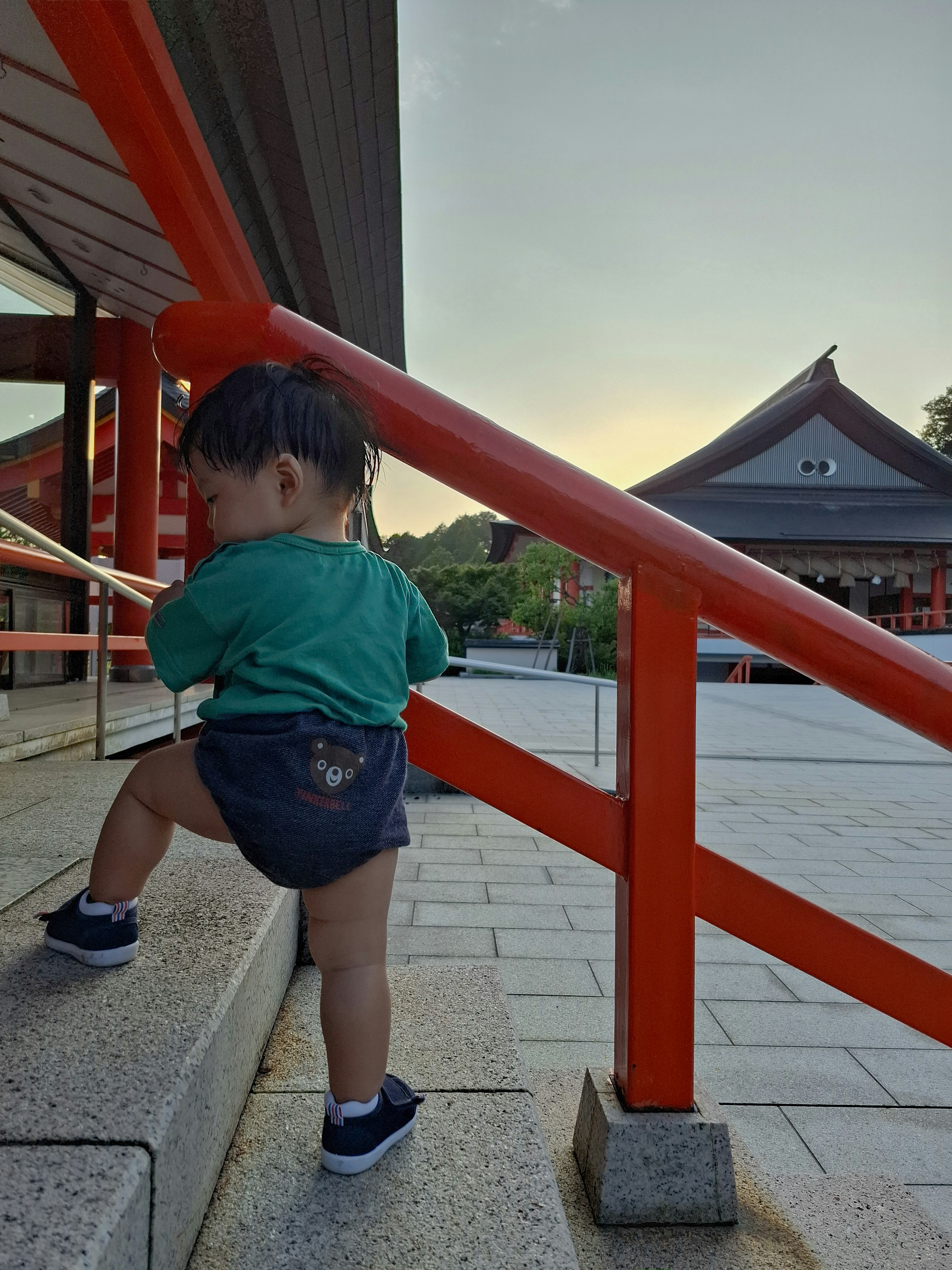 孩子在日落時分於神社的紅色扶手旁爬樓梯