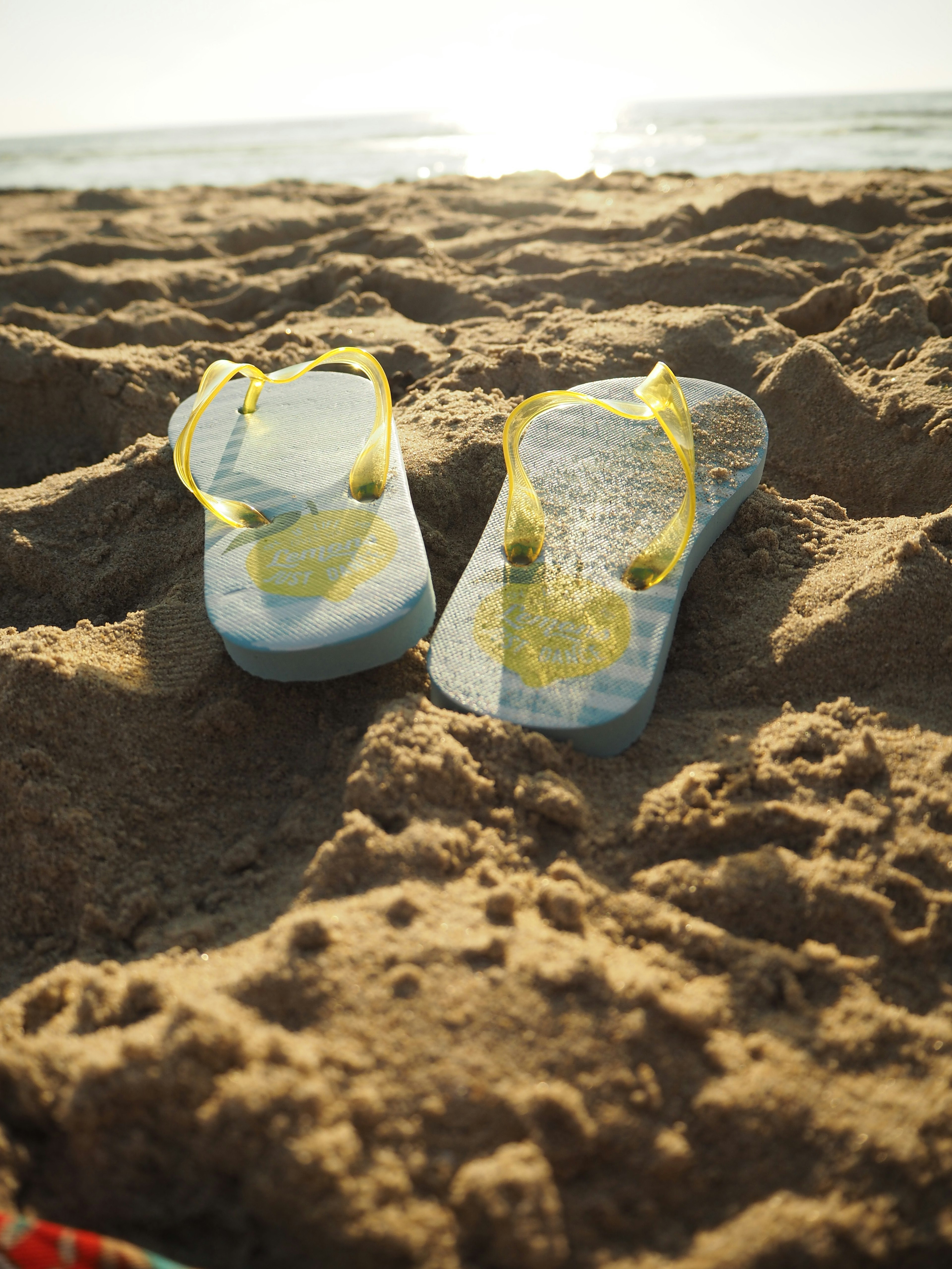 Sandalnya biru dengan tali kuning di pantai berpasir