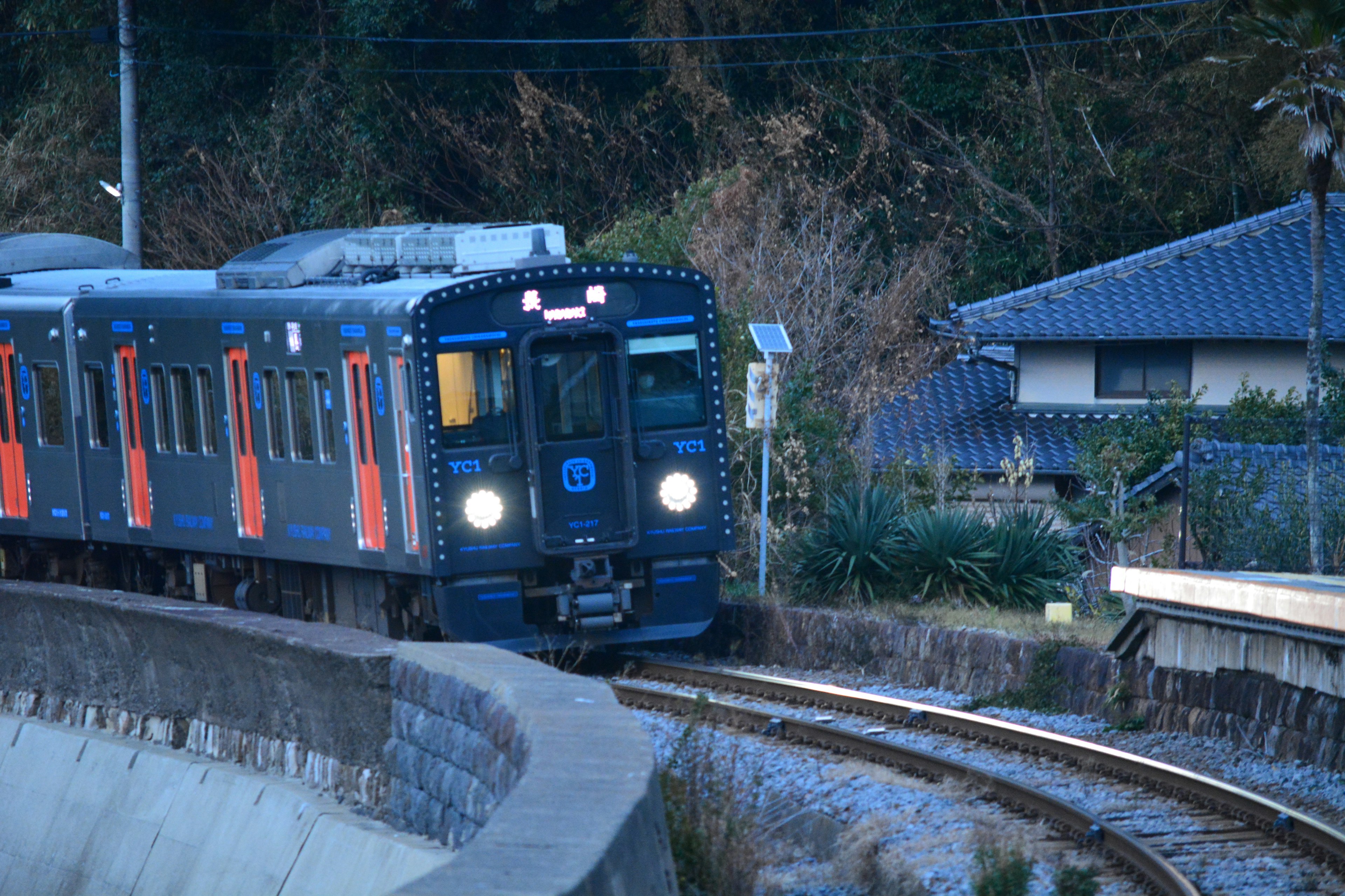 Blue train rounding a bend with houses visible in the background