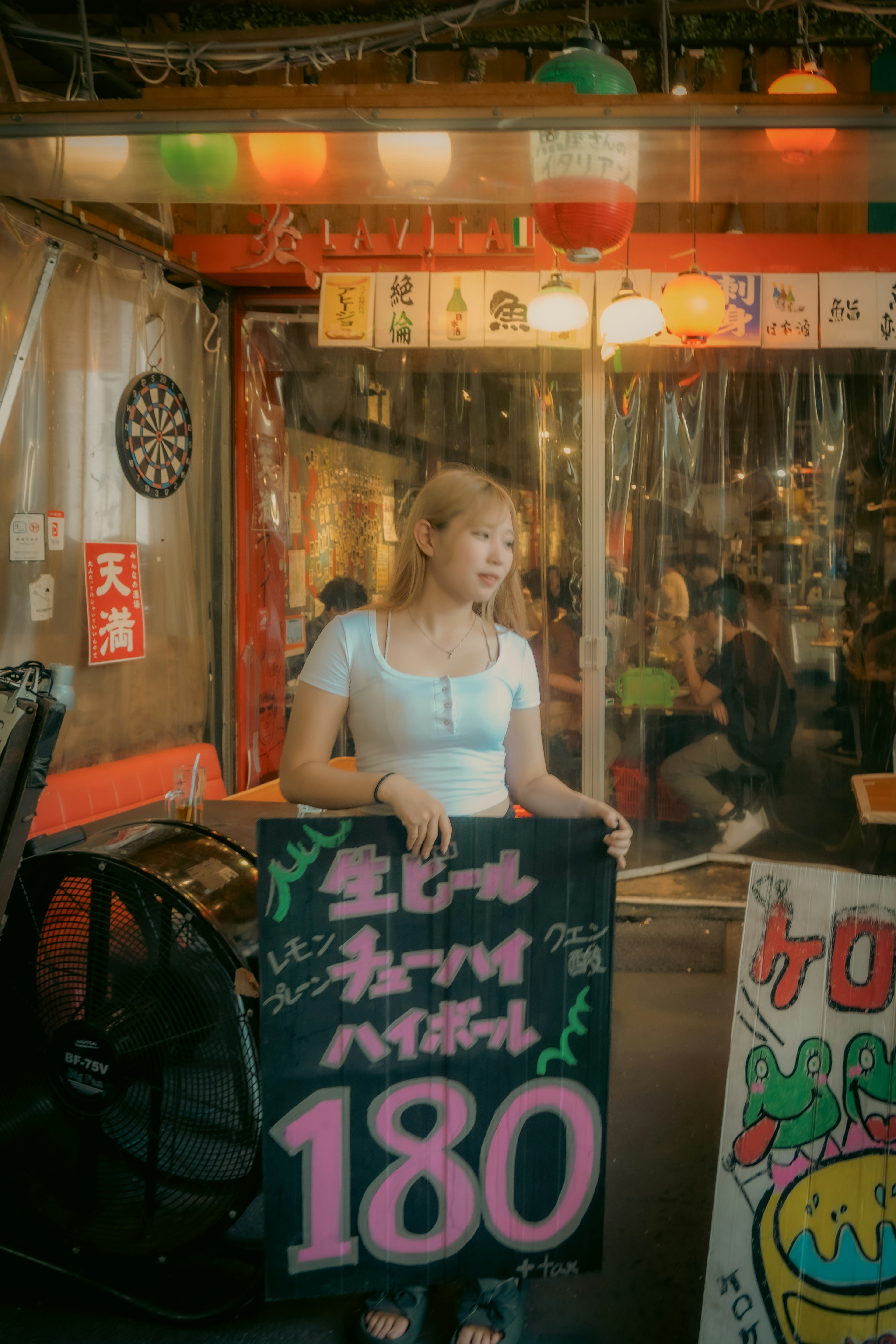 Young woman holding a colorful sign in a vibrant izakaya interior