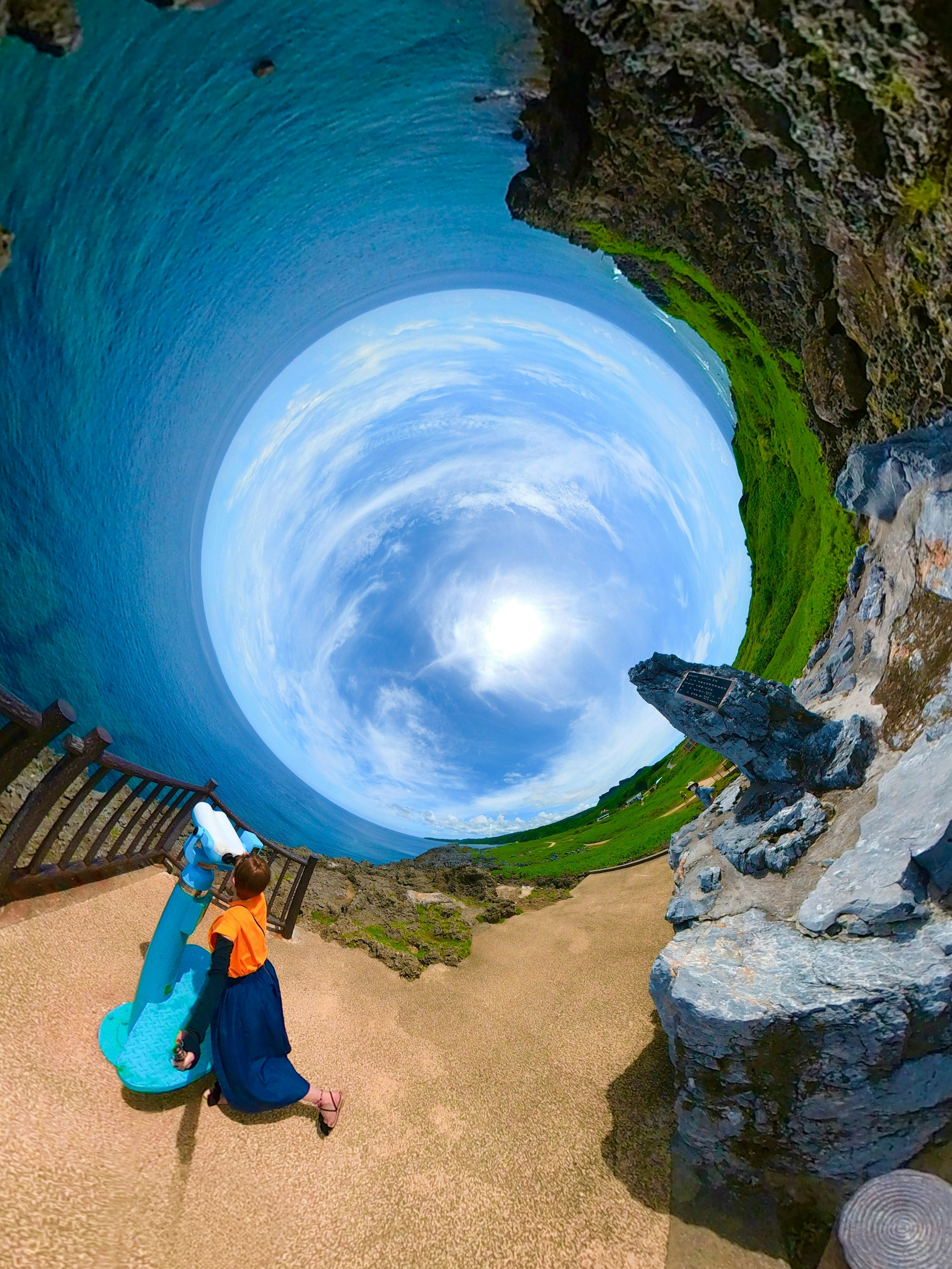 Una donna in abiti blu che cammina in un paesaggio con cielo blu e campi verdi