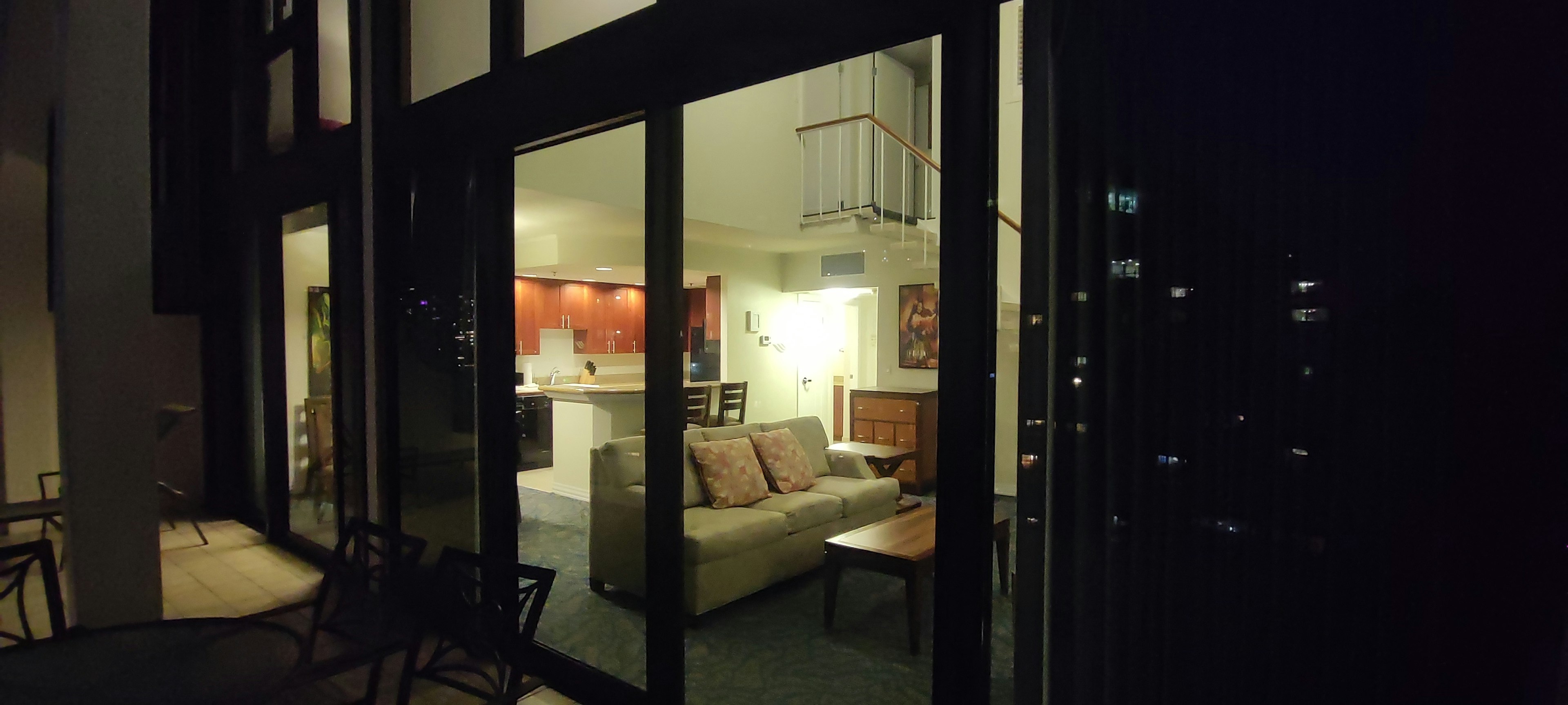 View of living room at night through large glass door featuring a bright sofa and dining area