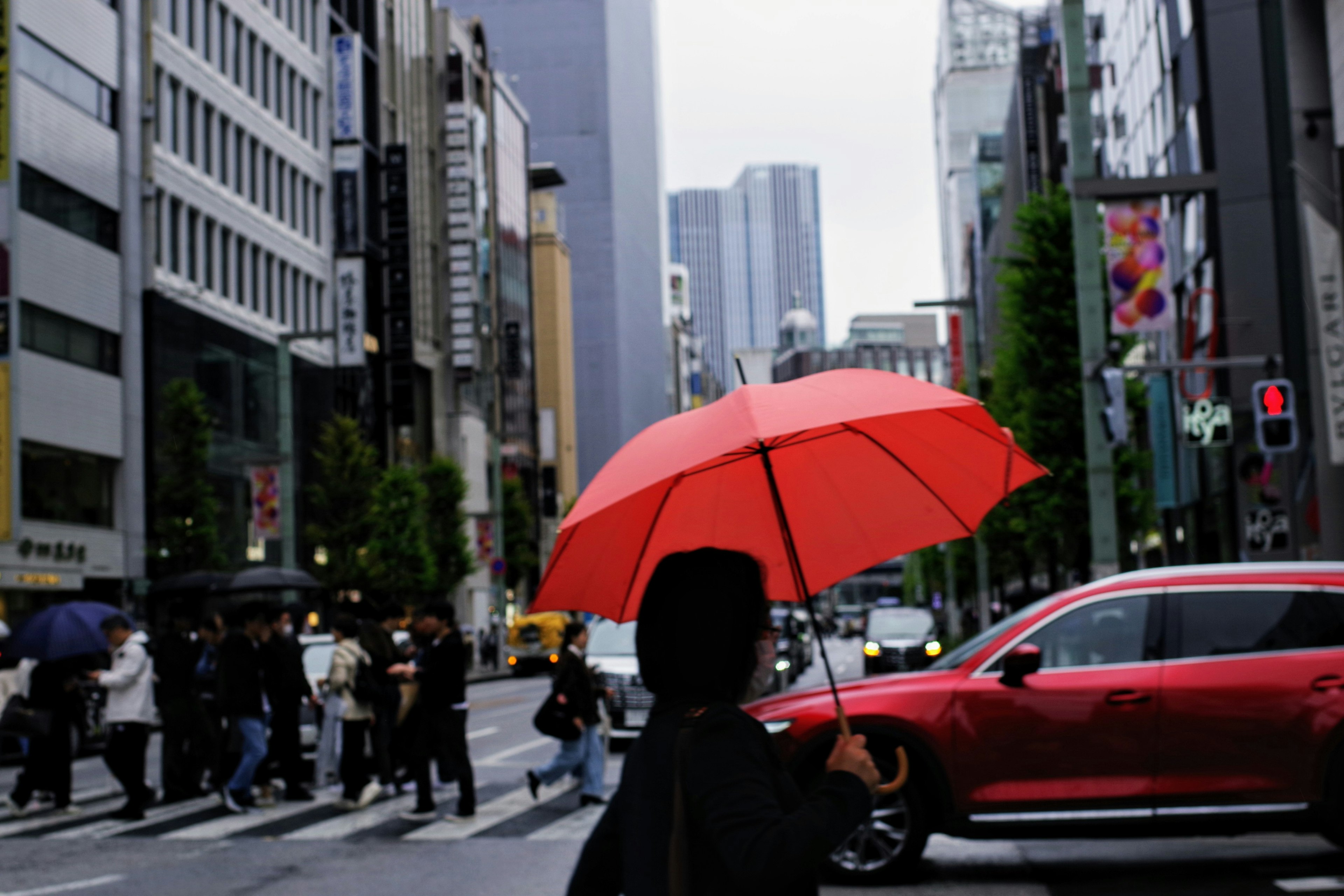 赤い傘を持つ人が街を歩く風景 高層ビルと車が見える