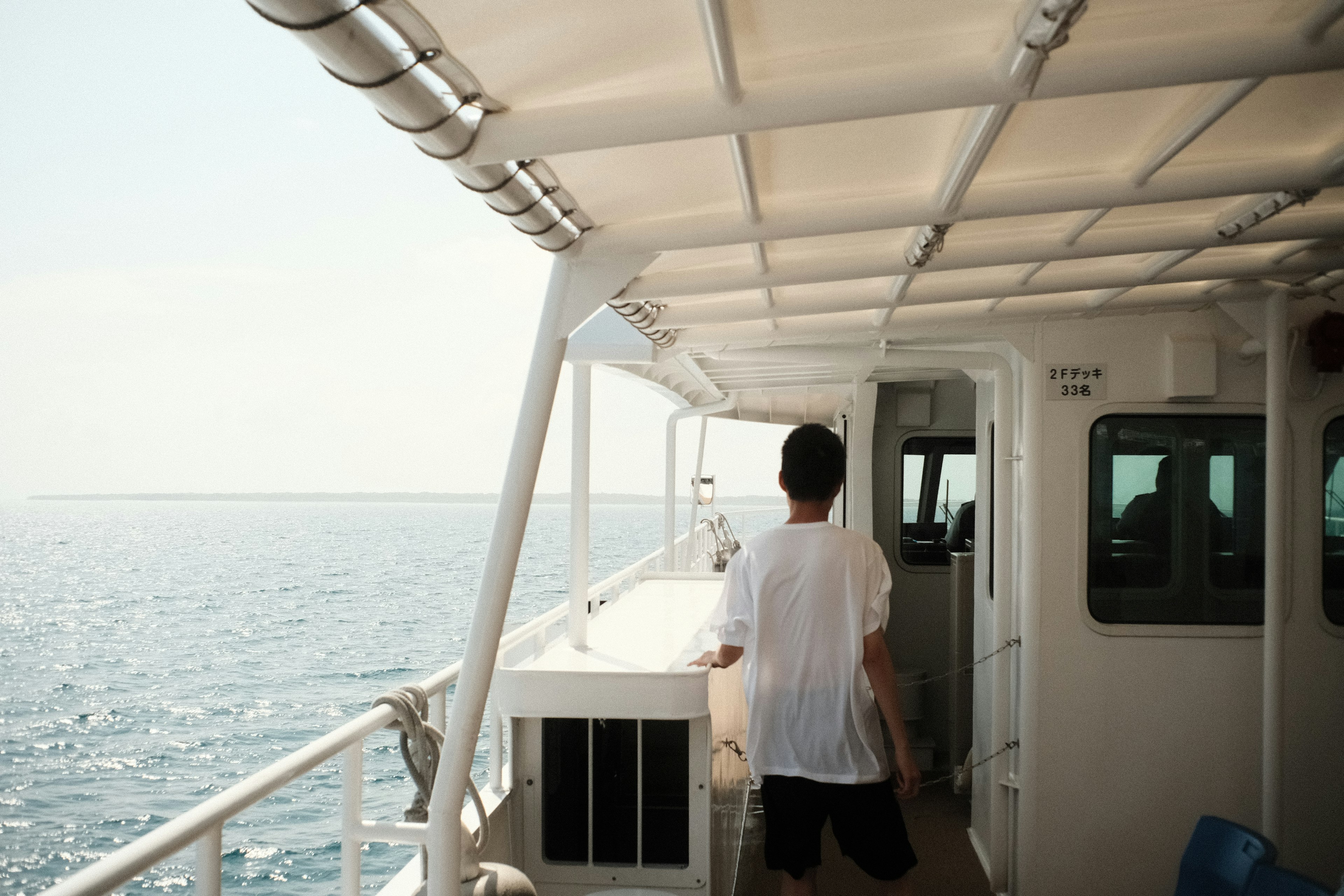 海の上を歩く男性の後ろ姿 船のデッキと明るい空