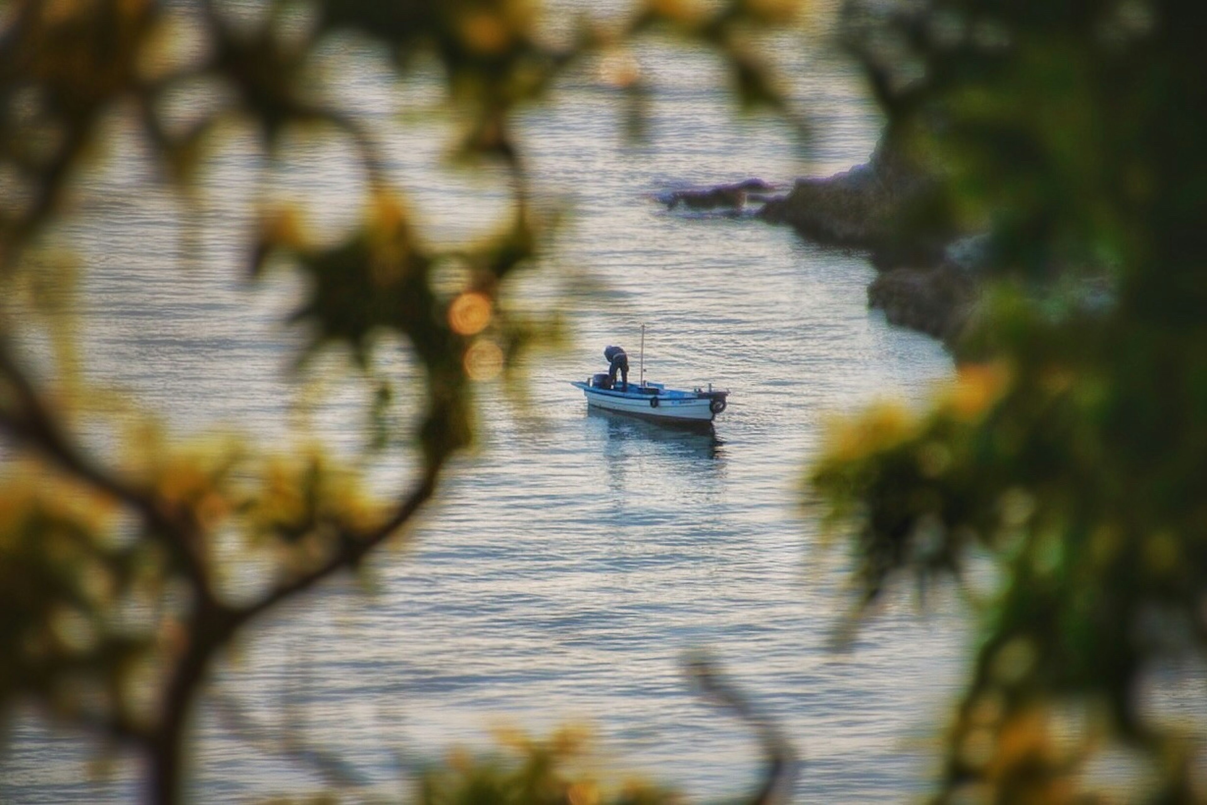 เงาของชาวประมงในเรือเล็กบนผิวน้ำที่สงบ