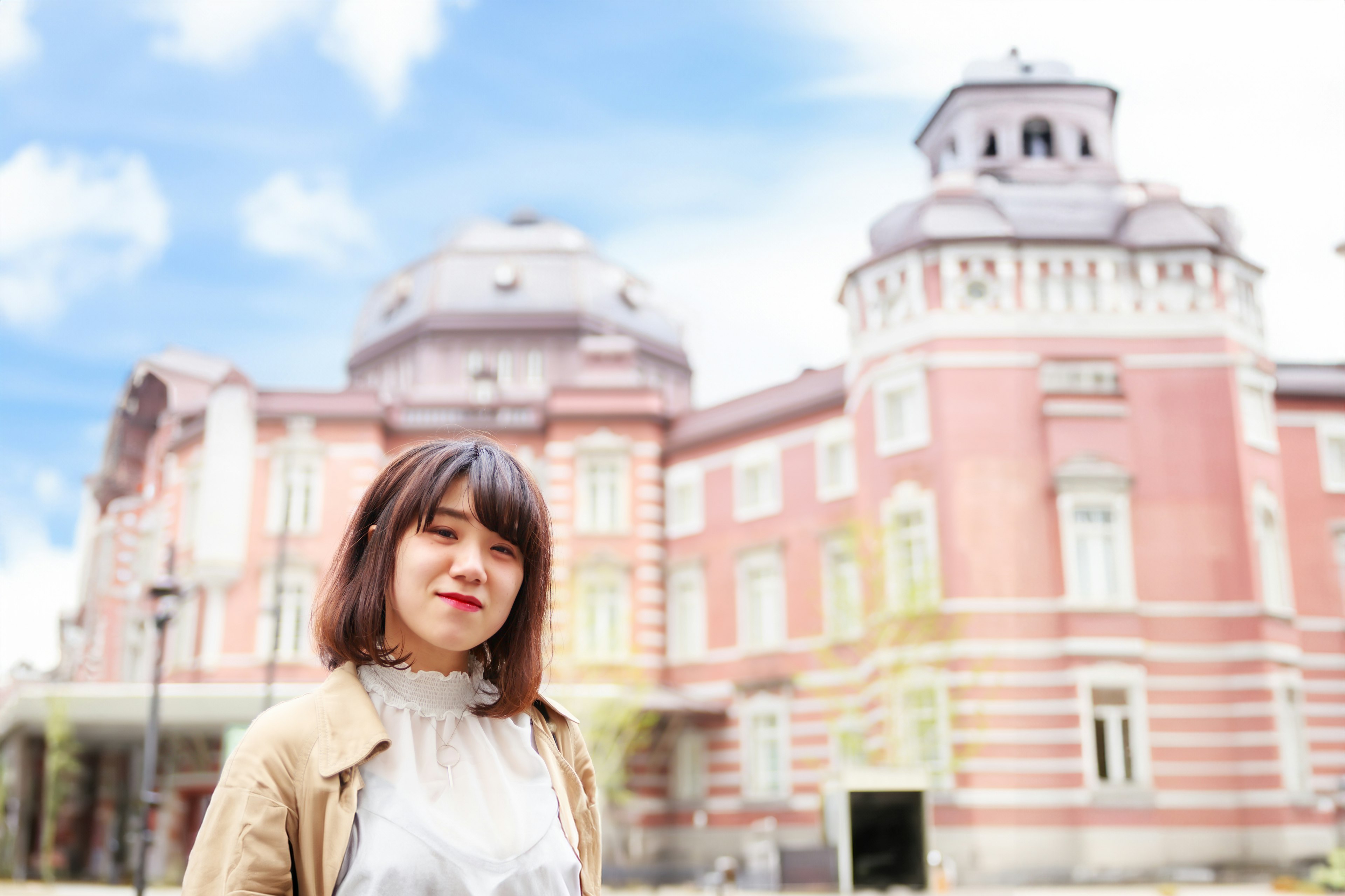 A woman smiling in front of Tokyo Station in a bright photo