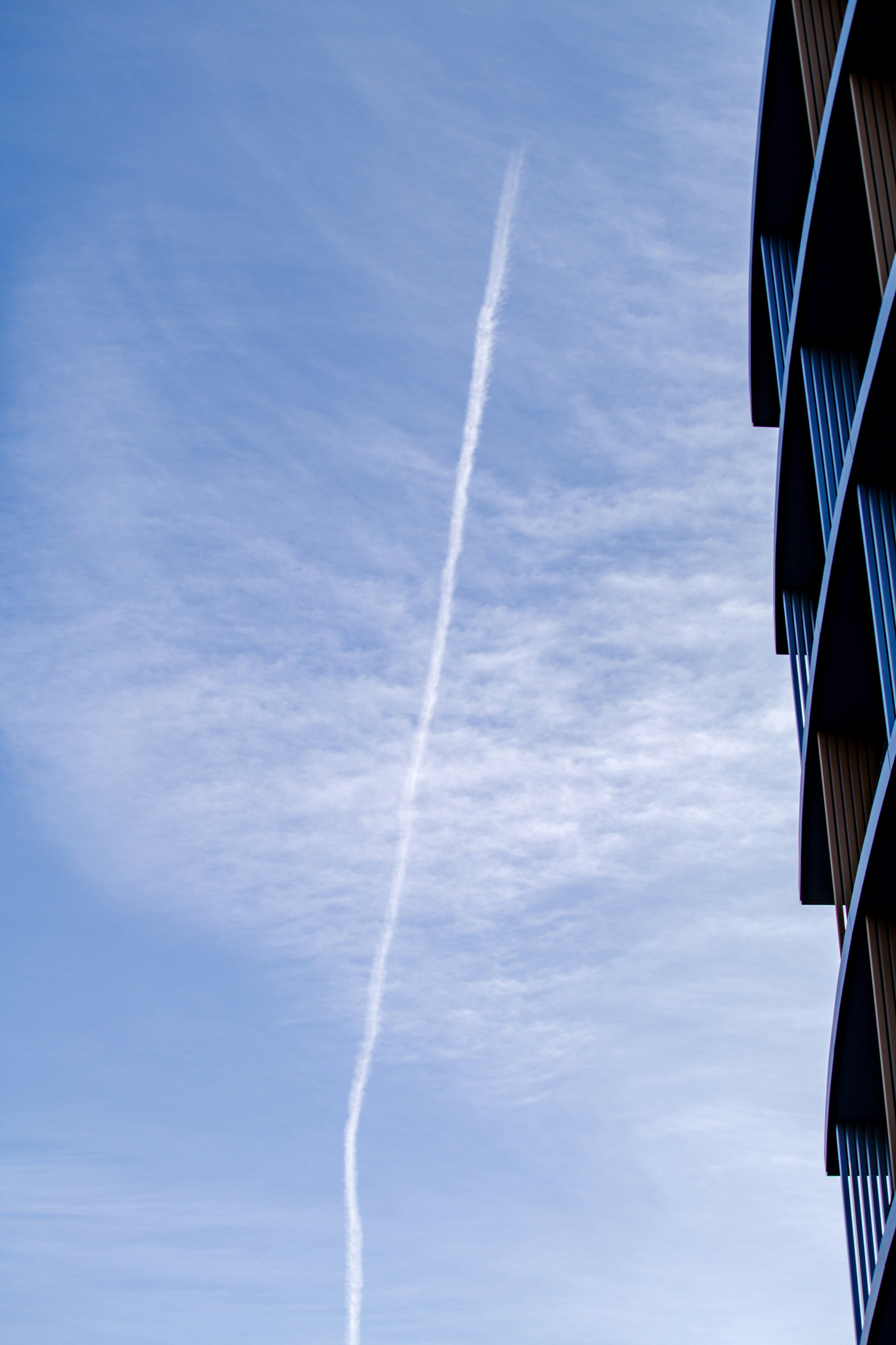 Estela blanca extendiéndose en un cielo azul junto a un edificio