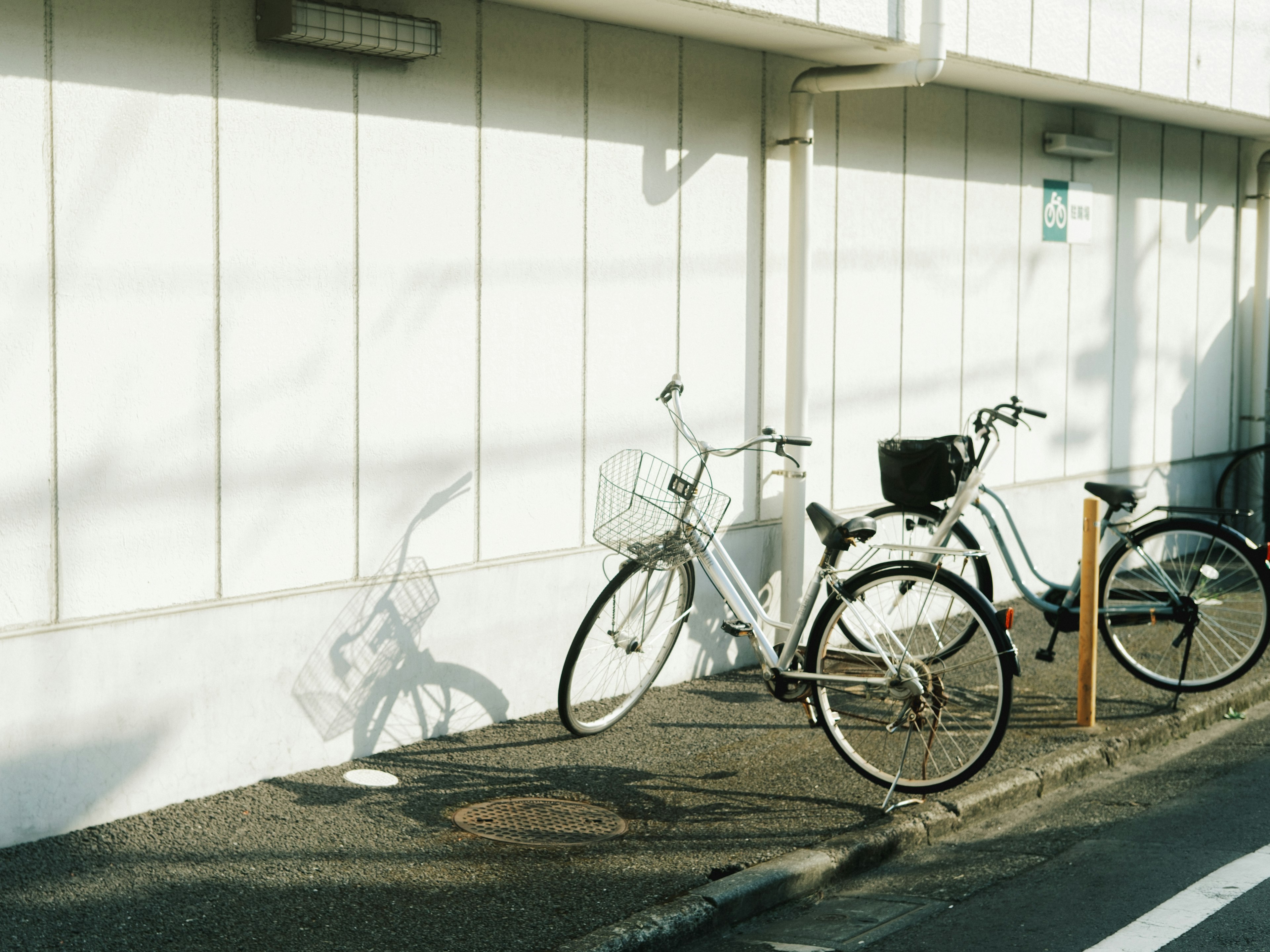 Two bicycles leaning against a wall with shadows on the ground