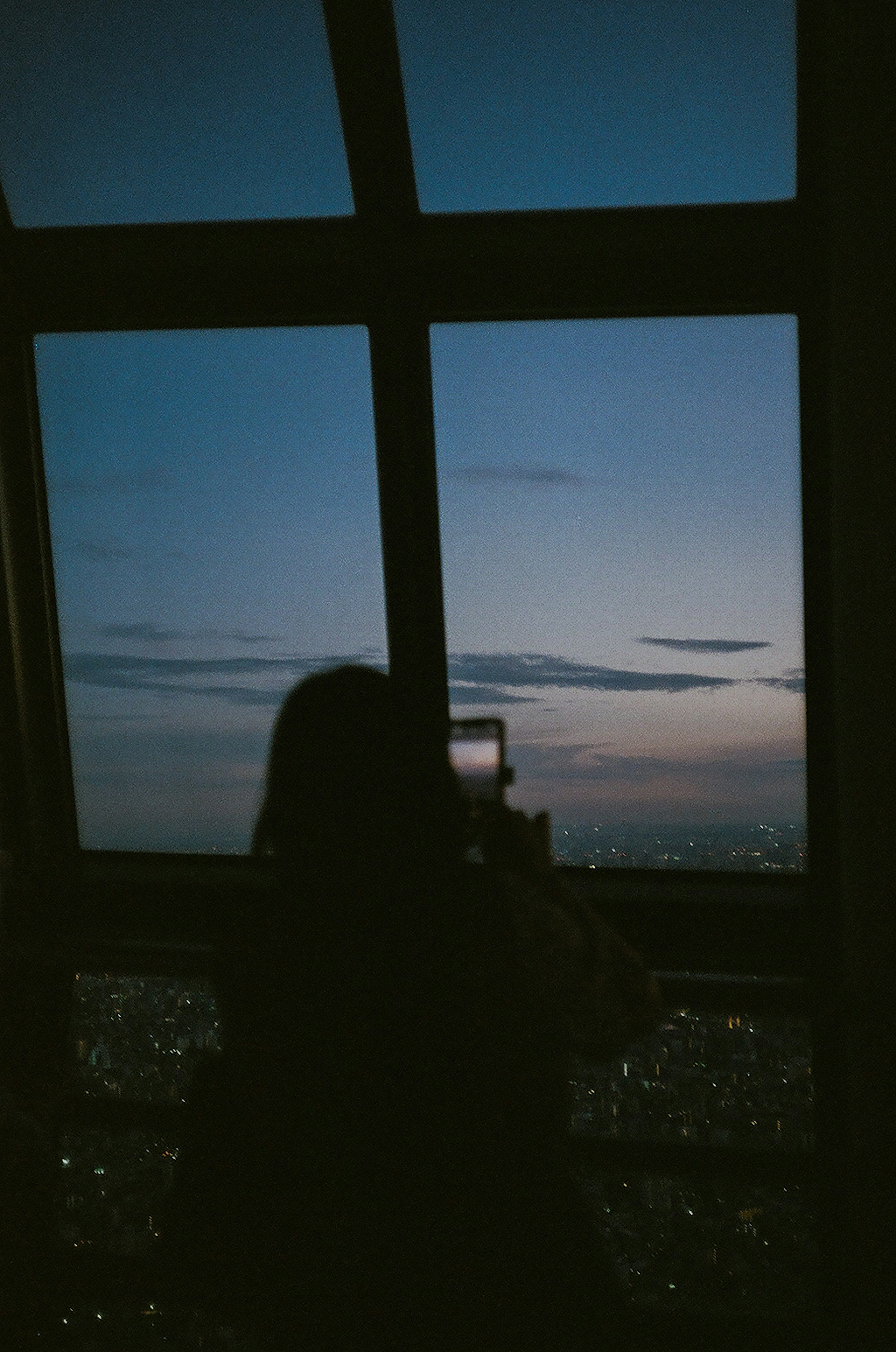 Silhouette of a person taking a photo of the sunset view through a window