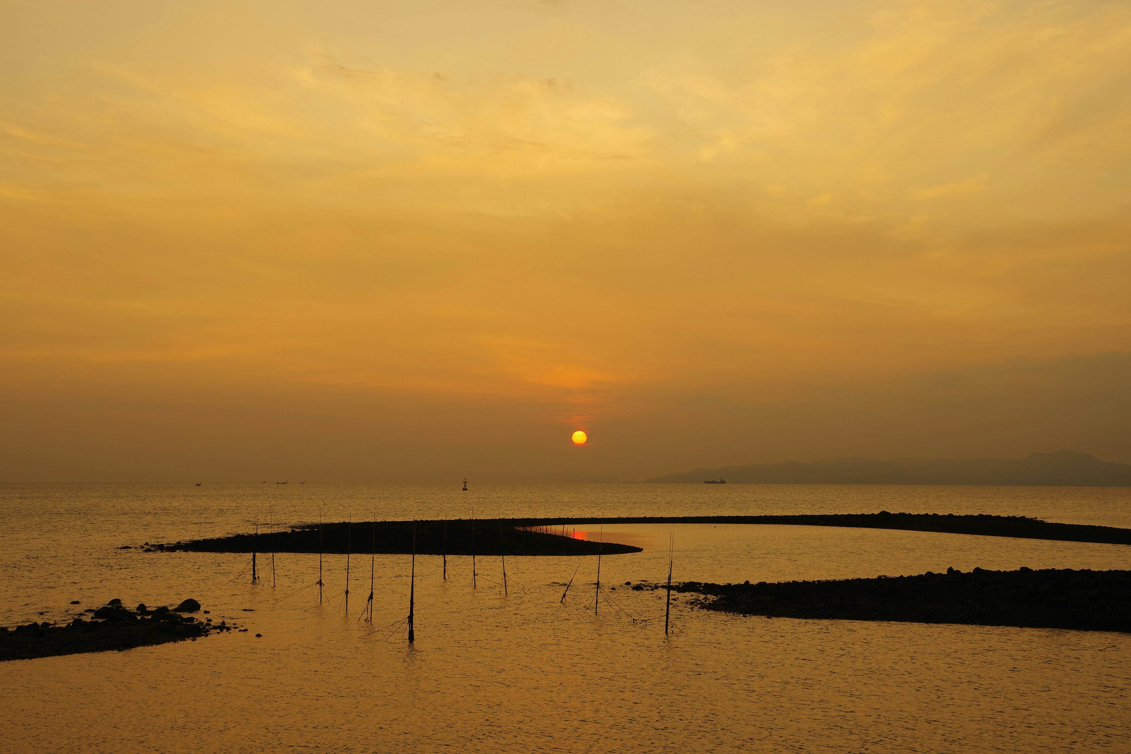 Tramonto sul mare calmo con sfumature arancioni e isole in silhouette