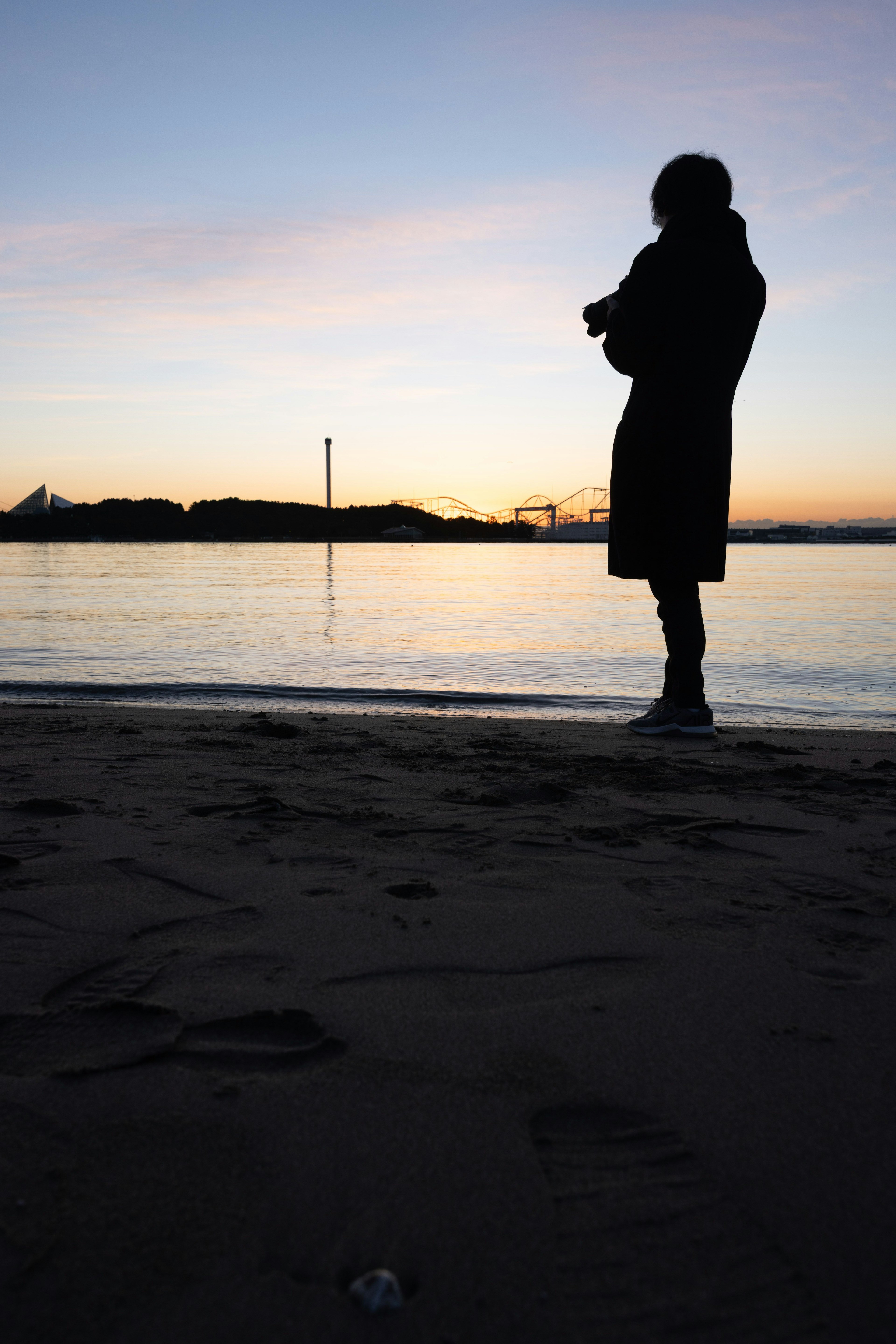 夕暮れ時の海辺でシルエットの人物が立っている