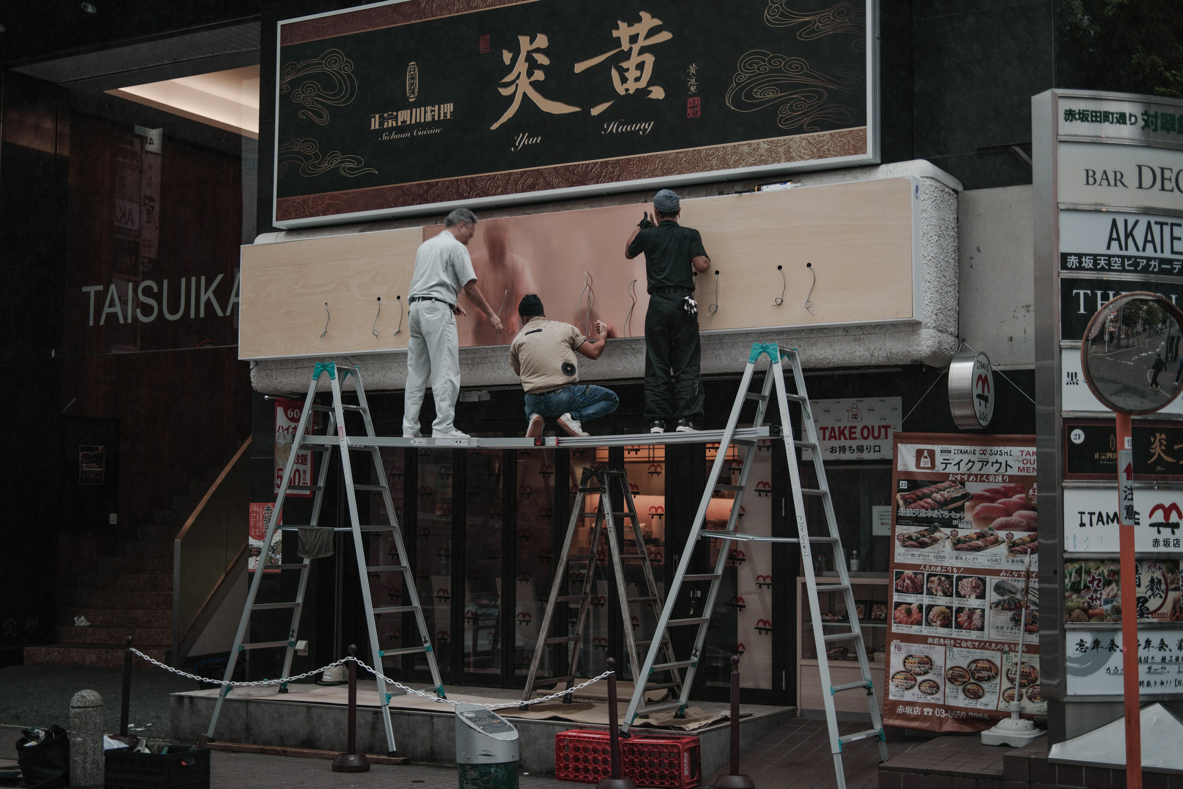 Trabajadores instalando un letrero en un andamio frente a un restaurante