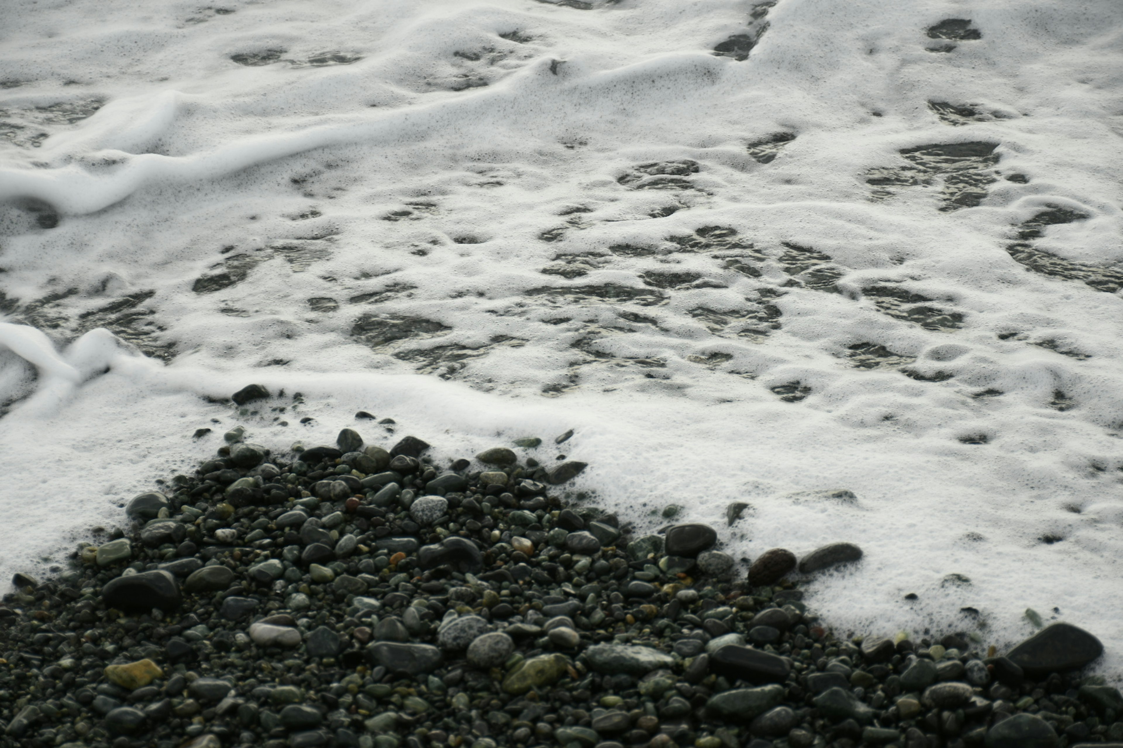 Onde oceaniche che si infrangono su ciottoli con schiuma bianca