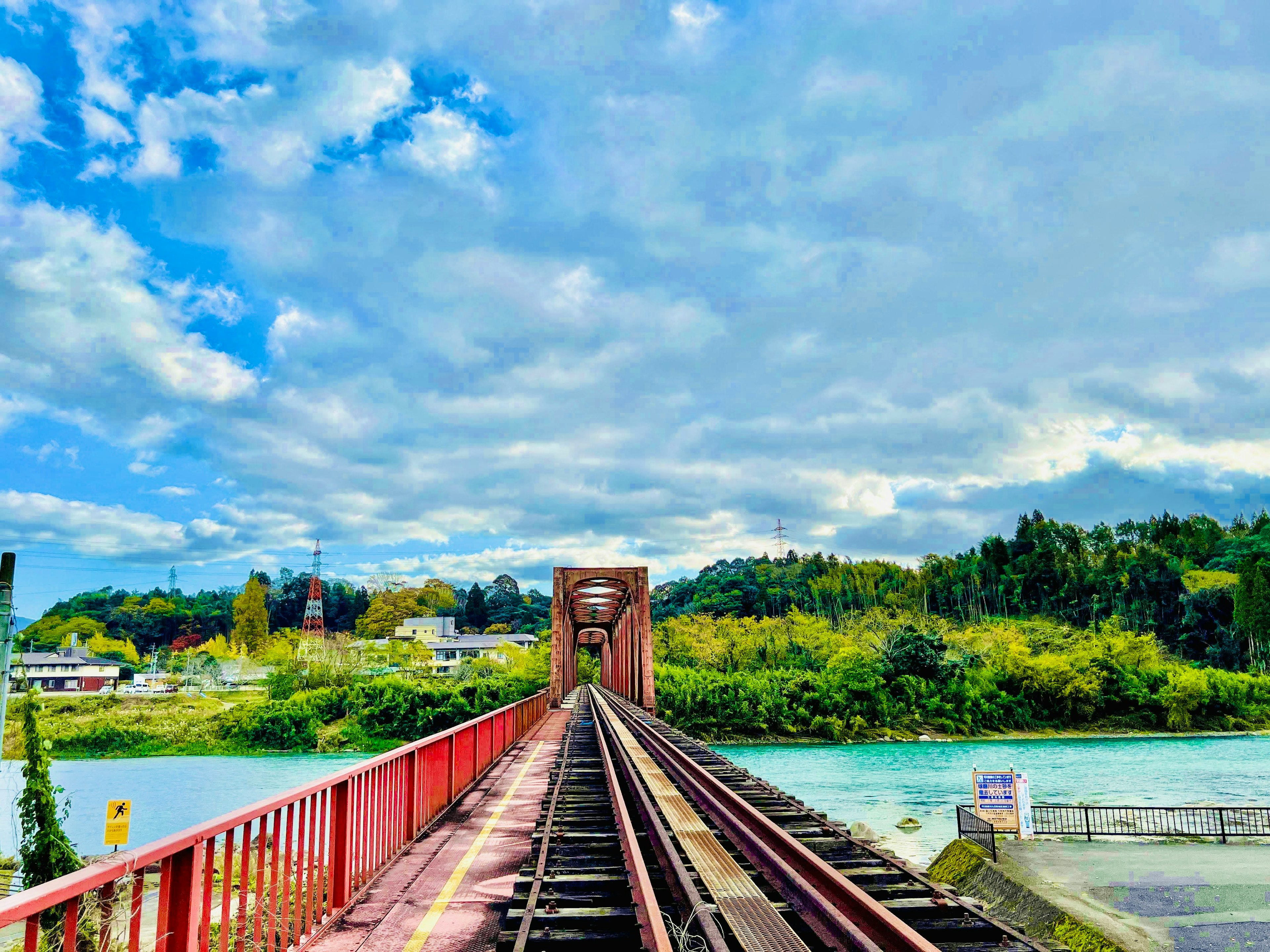 Rote Eisenbahnbrücke mit blauem Himmel und grünen Bäumen entlang des Flusses