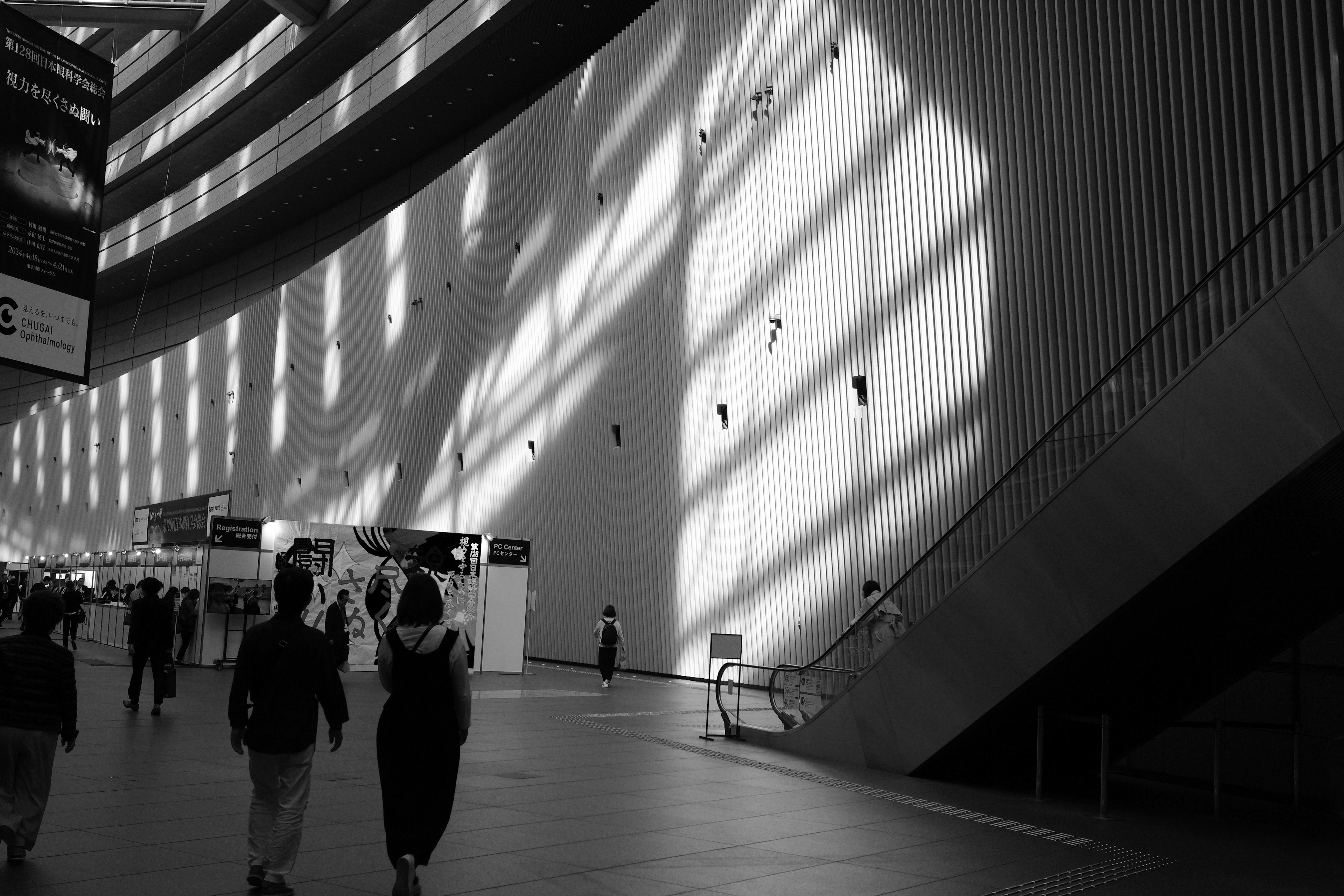 Black and white interior of a building with shadows on the wall and people walking