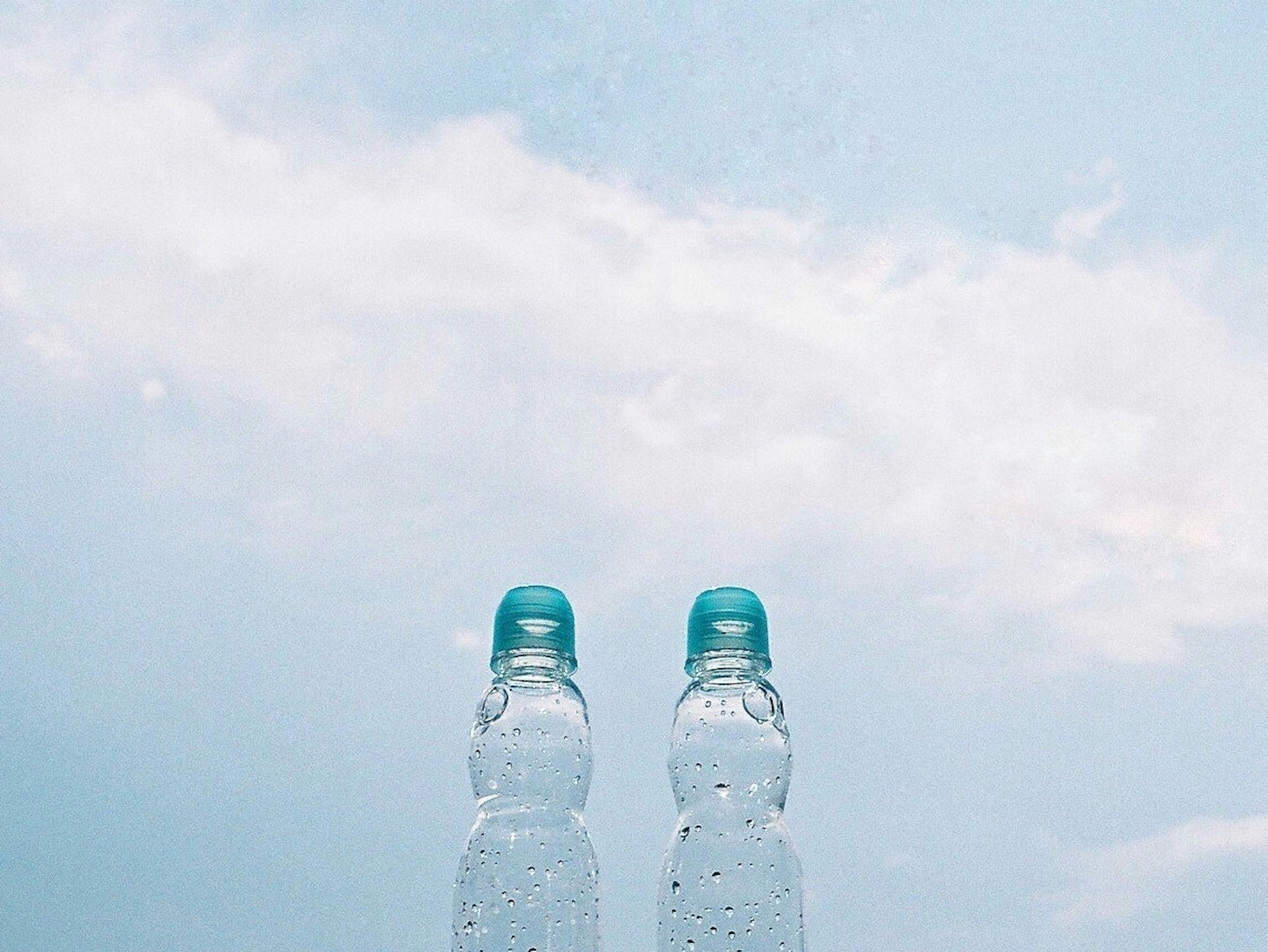 Two water bottles with blue caps against a light blue sky