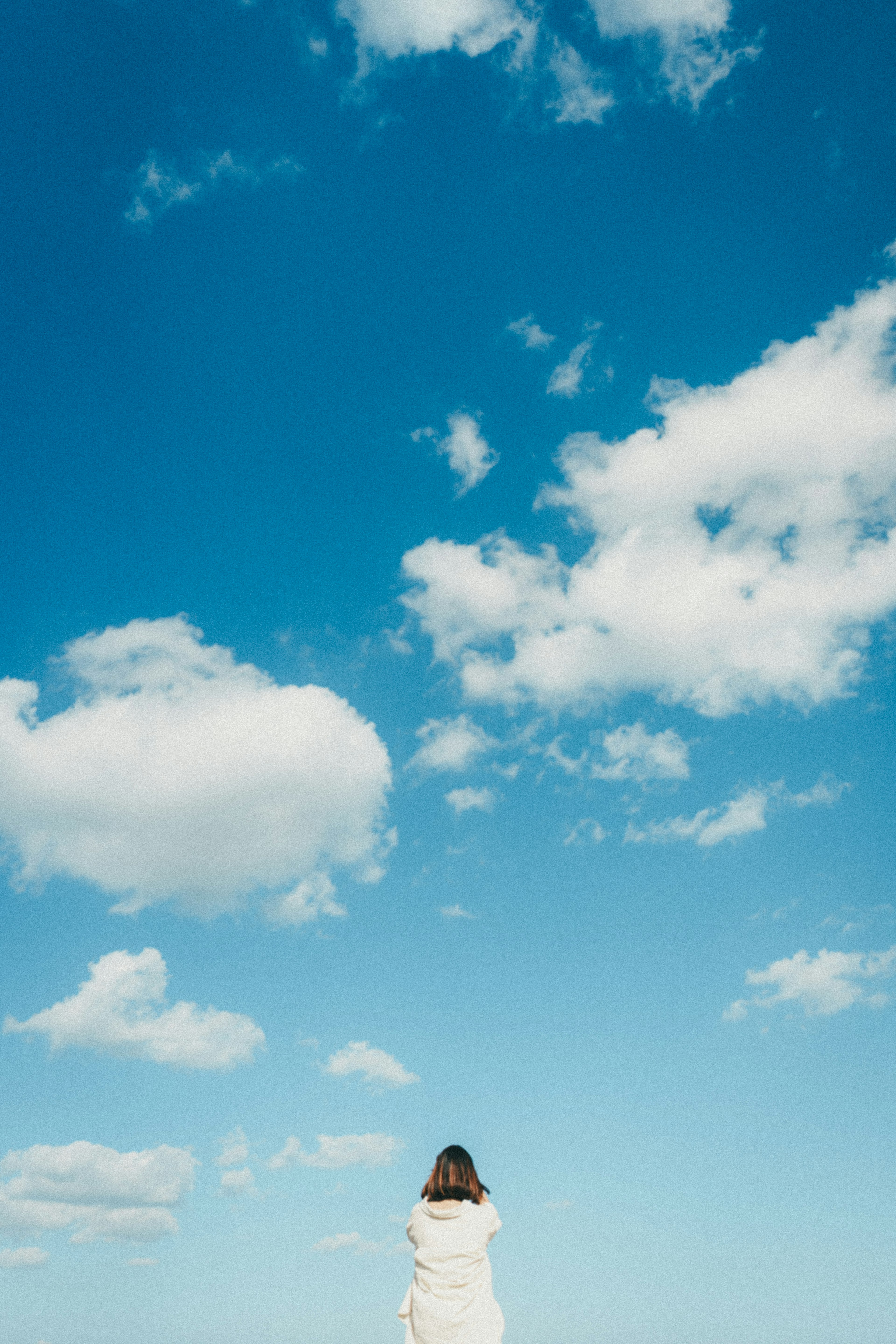 Mujer de pie bajo un cielo azul con nubes blancas