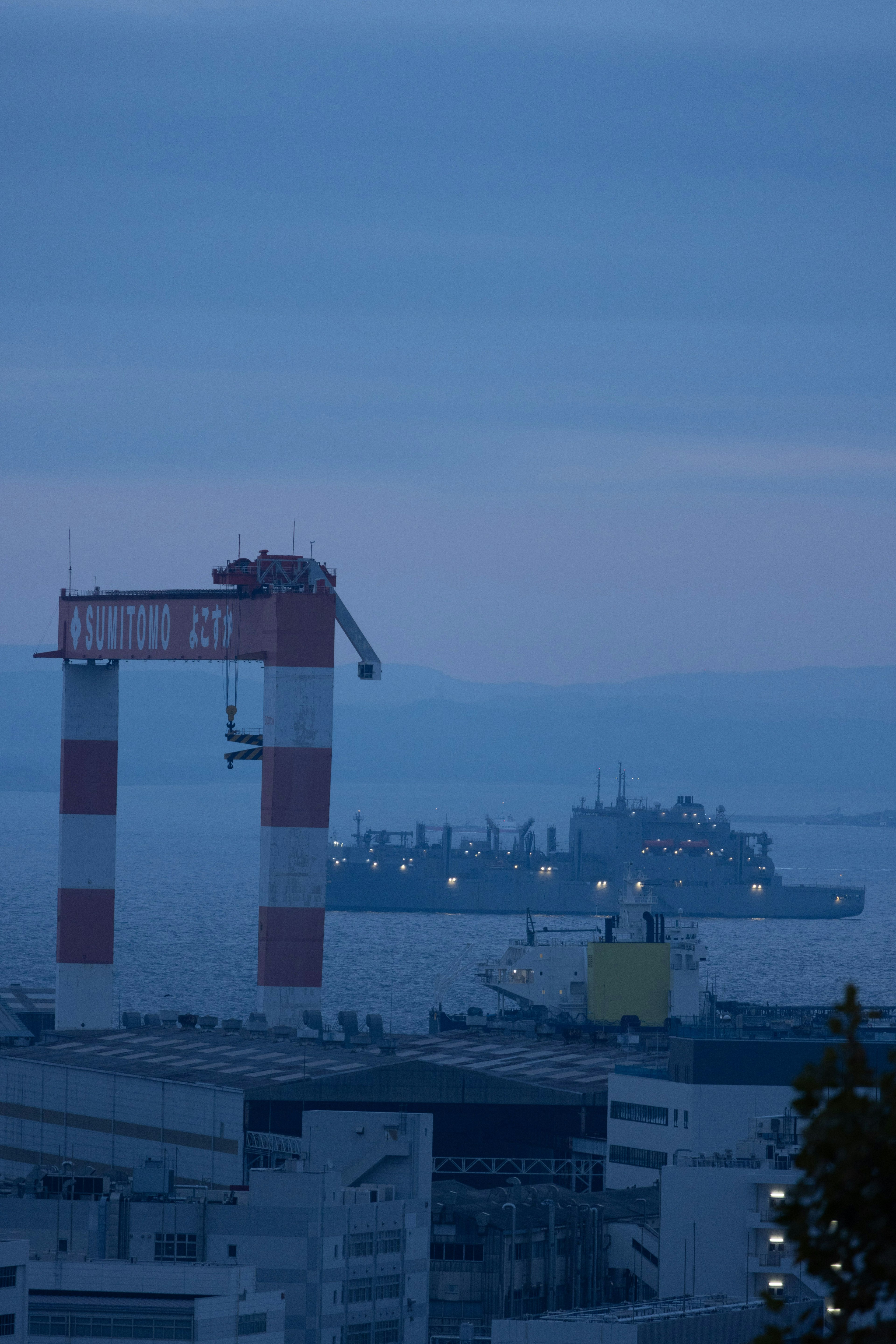 Ein Schiff auf einem blauen Dämmerungsmeer mit einem rot-weißen Kran im Vordergrund