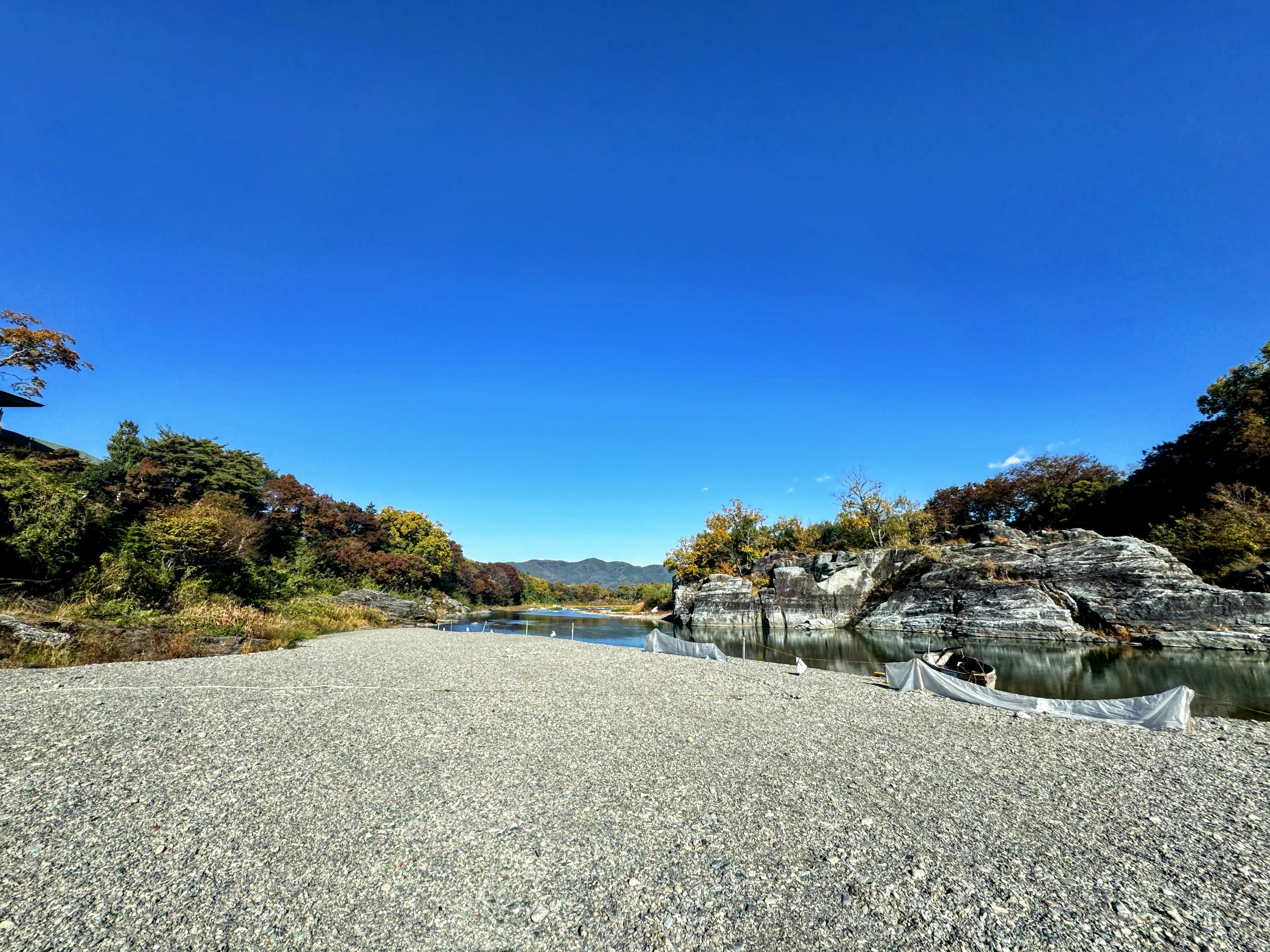 穏やかな川の景色と青空の広がり、石の多い砂利道