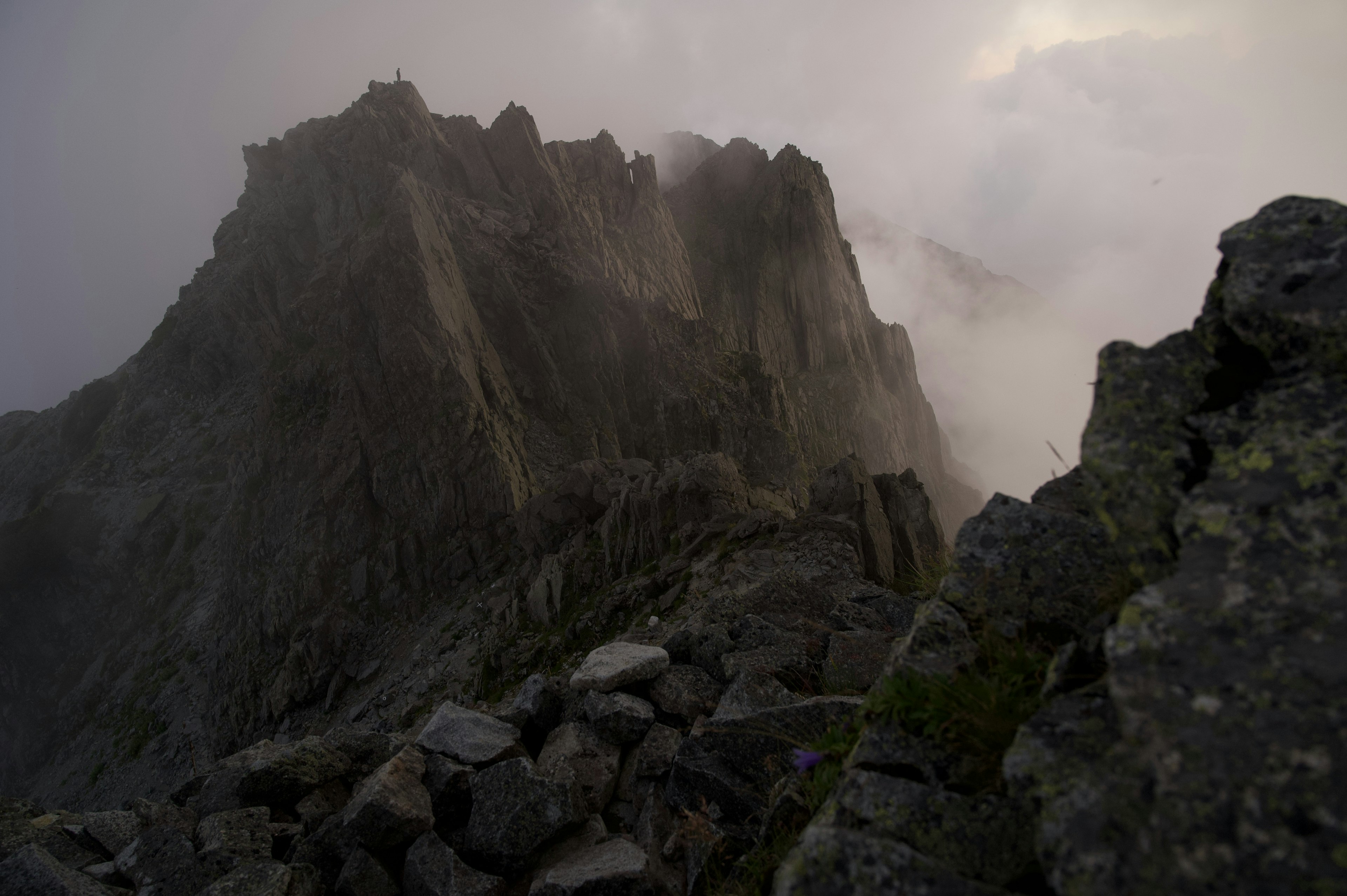 Paesaggio montano drammatico avvolto nella nebbia picchi rocciosi acuti e nuvole scure