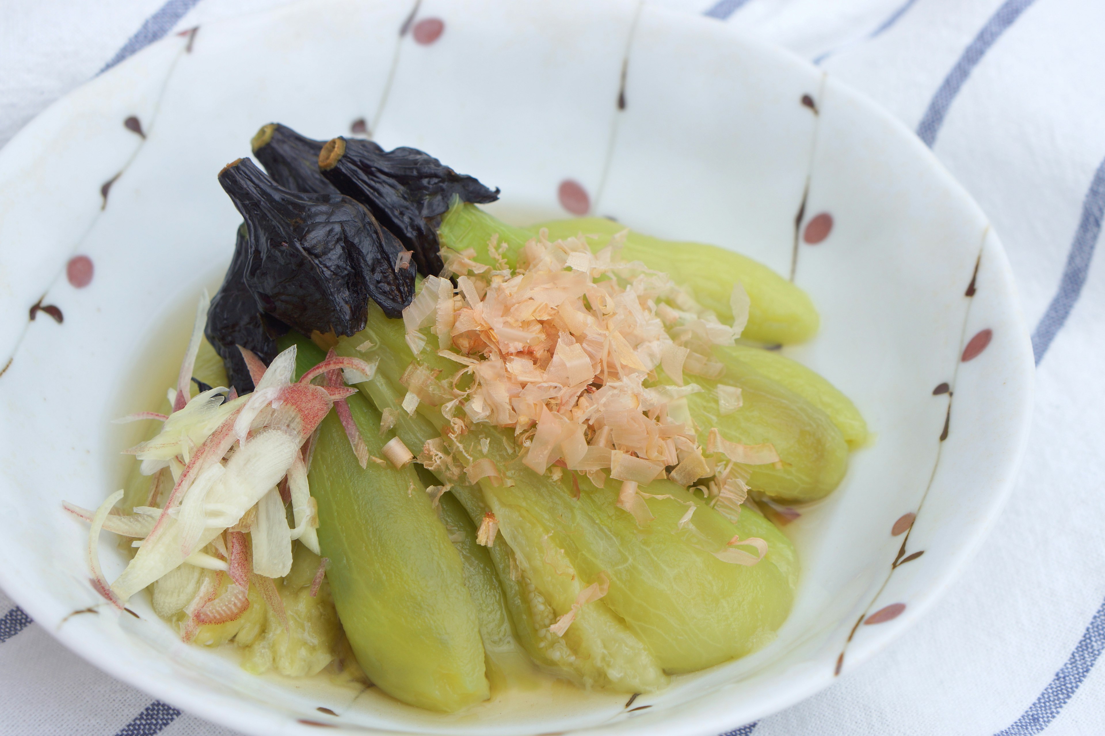 Plato de verduras verdes con hongo oscuro decorado con jengibre y chalotas fritas