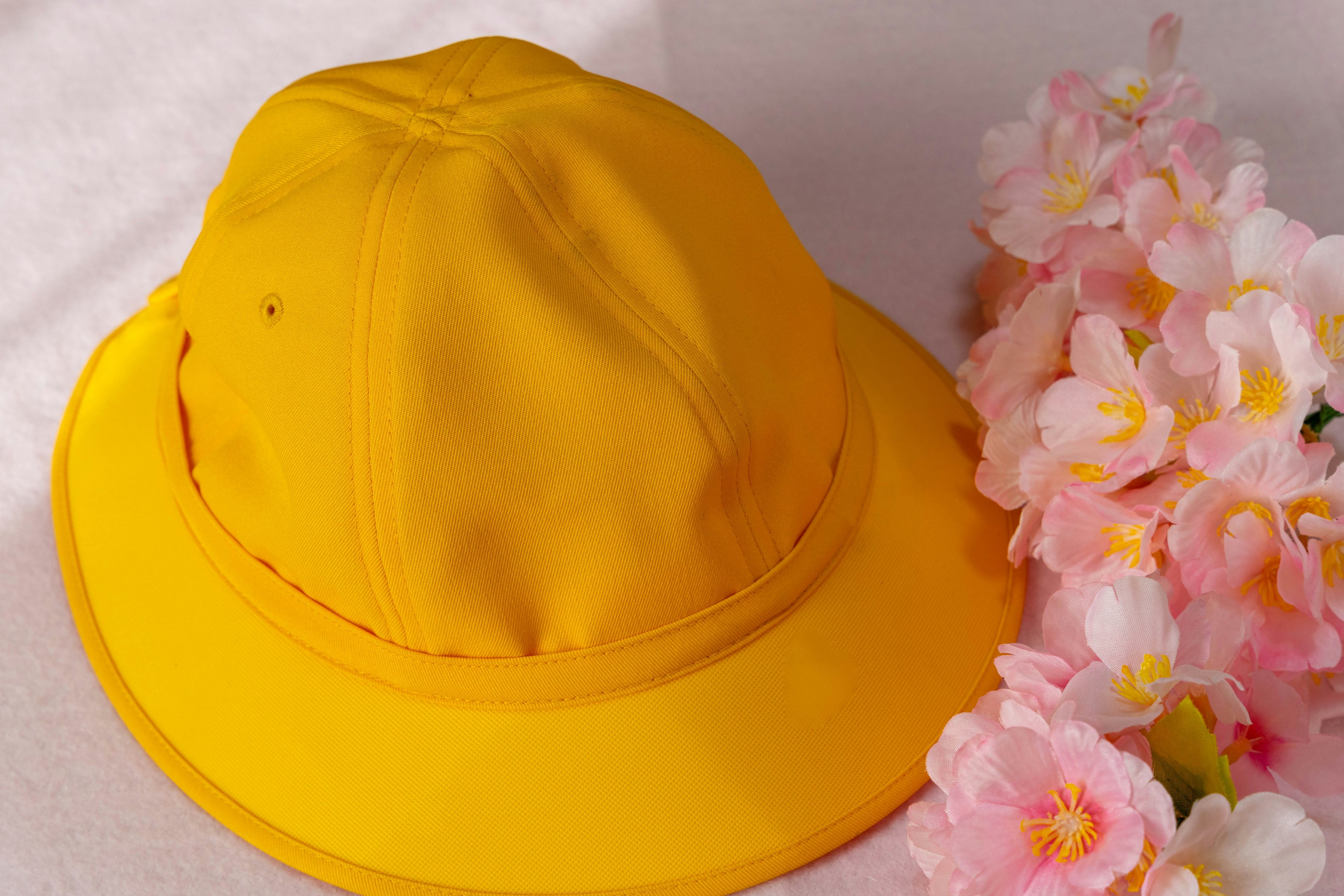 Cappello giallo accanto a decorazioni floreali rosa