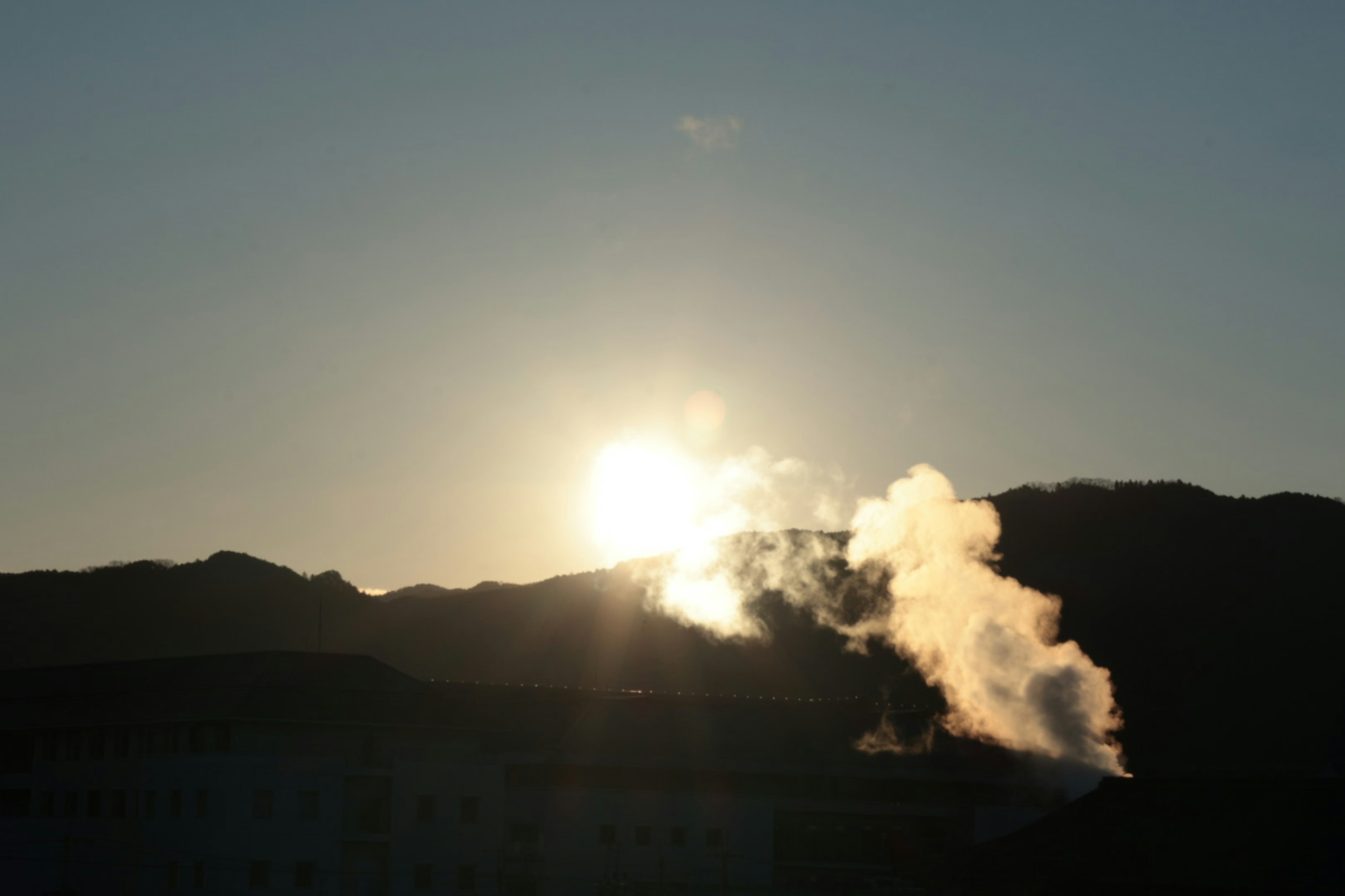 Coucher de soleil derrière les montagnes avec de la fumée s'élevant au premier plan