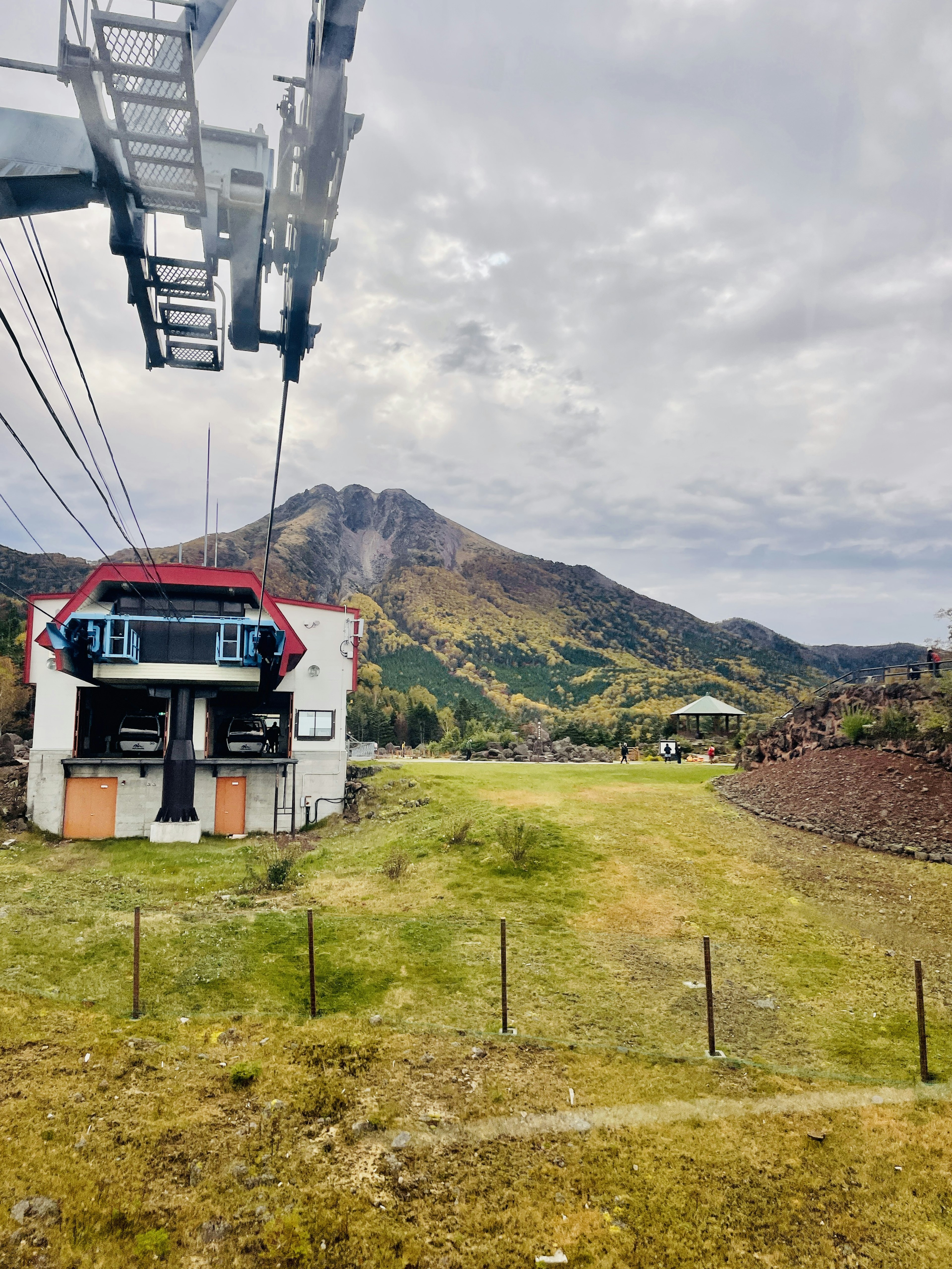 วิวภูเขากับสถานีเคเบิลคาร์และทุ่งหญ้าสีเขียวใต้ท้องฟ้าที่มีเมฆ