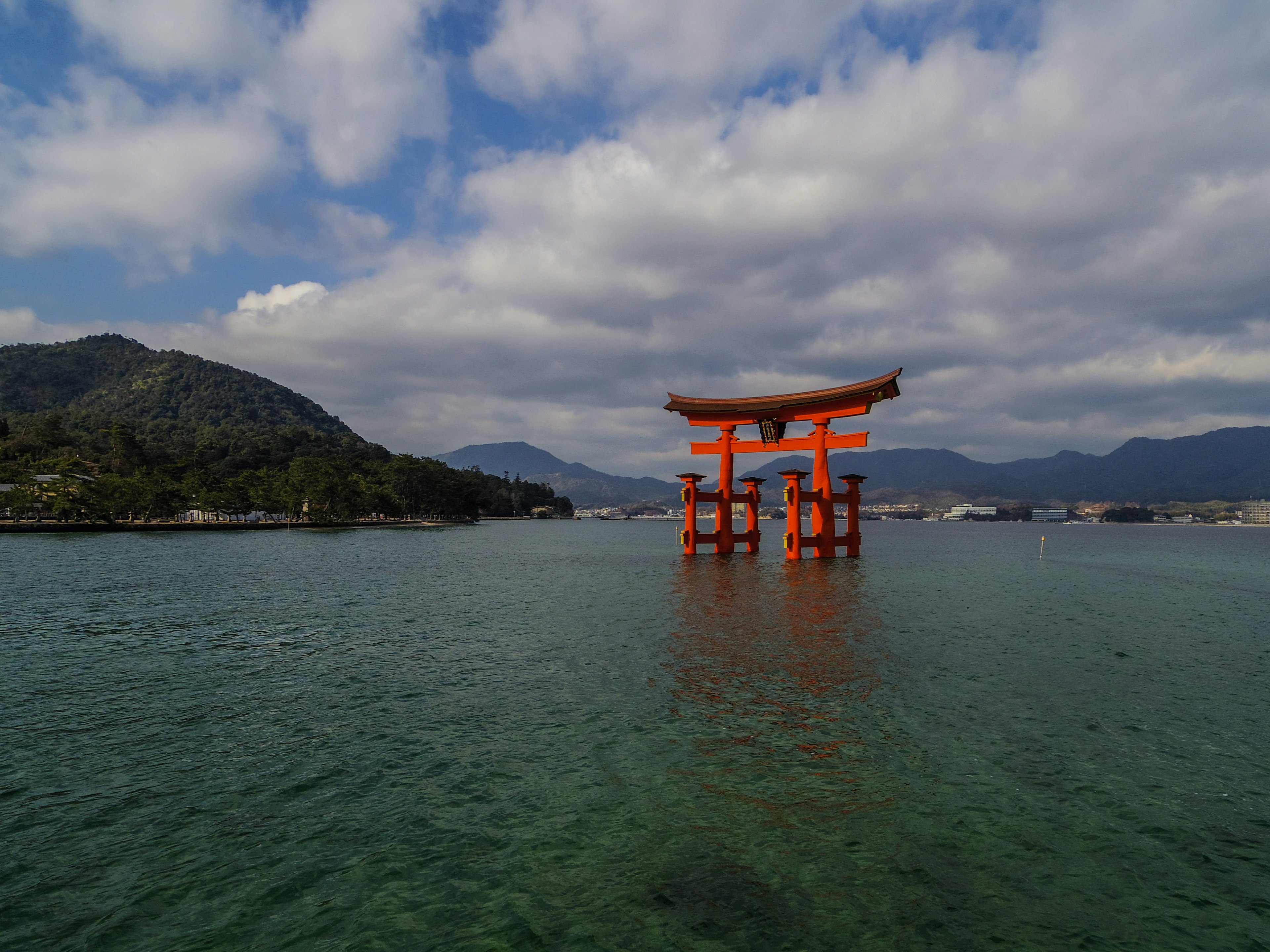 Cổng torii đỏ đứng trong nước với núi ở phía sau