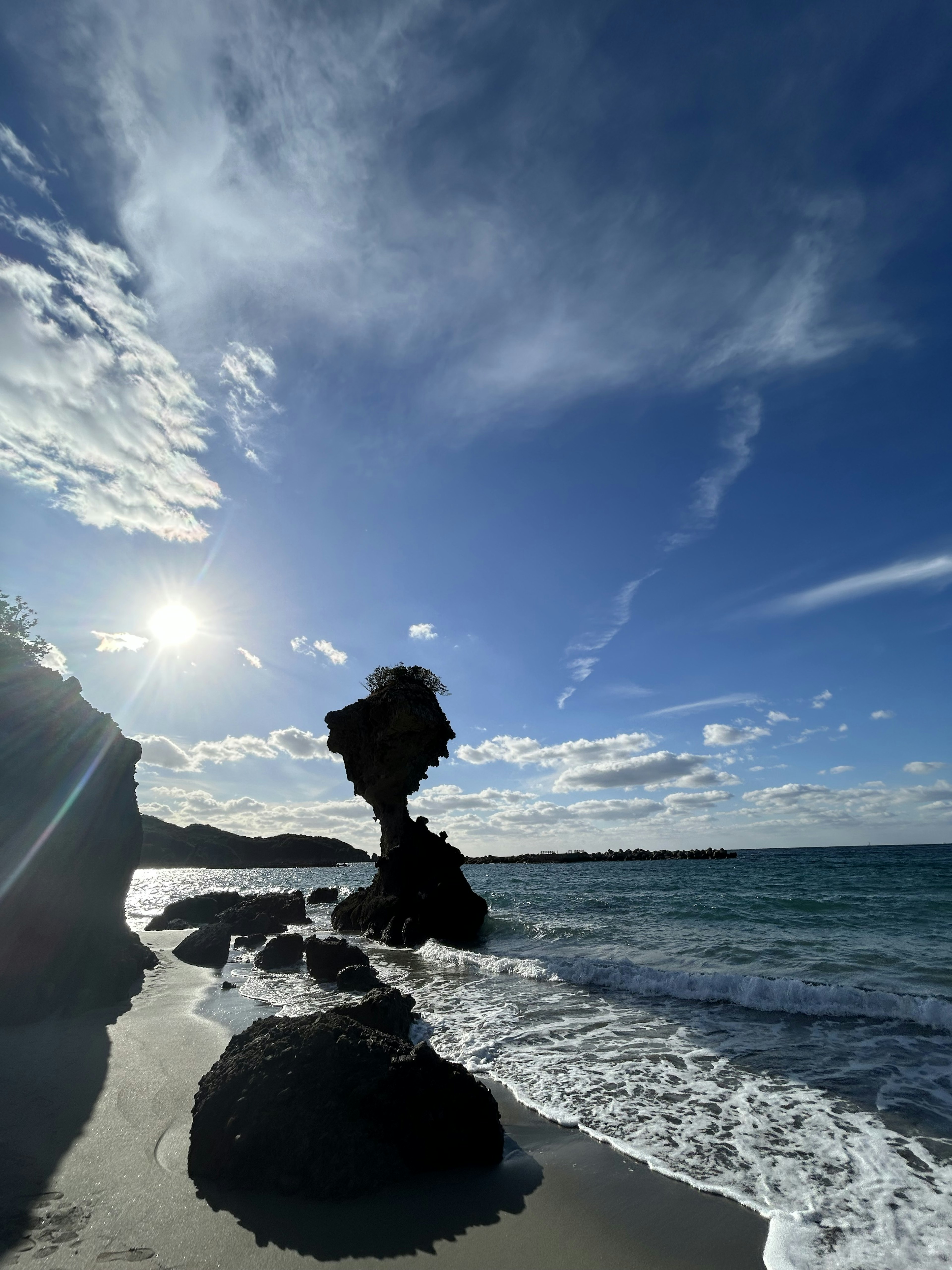 Silhouette of a unique rock formation against a blue sea and sky