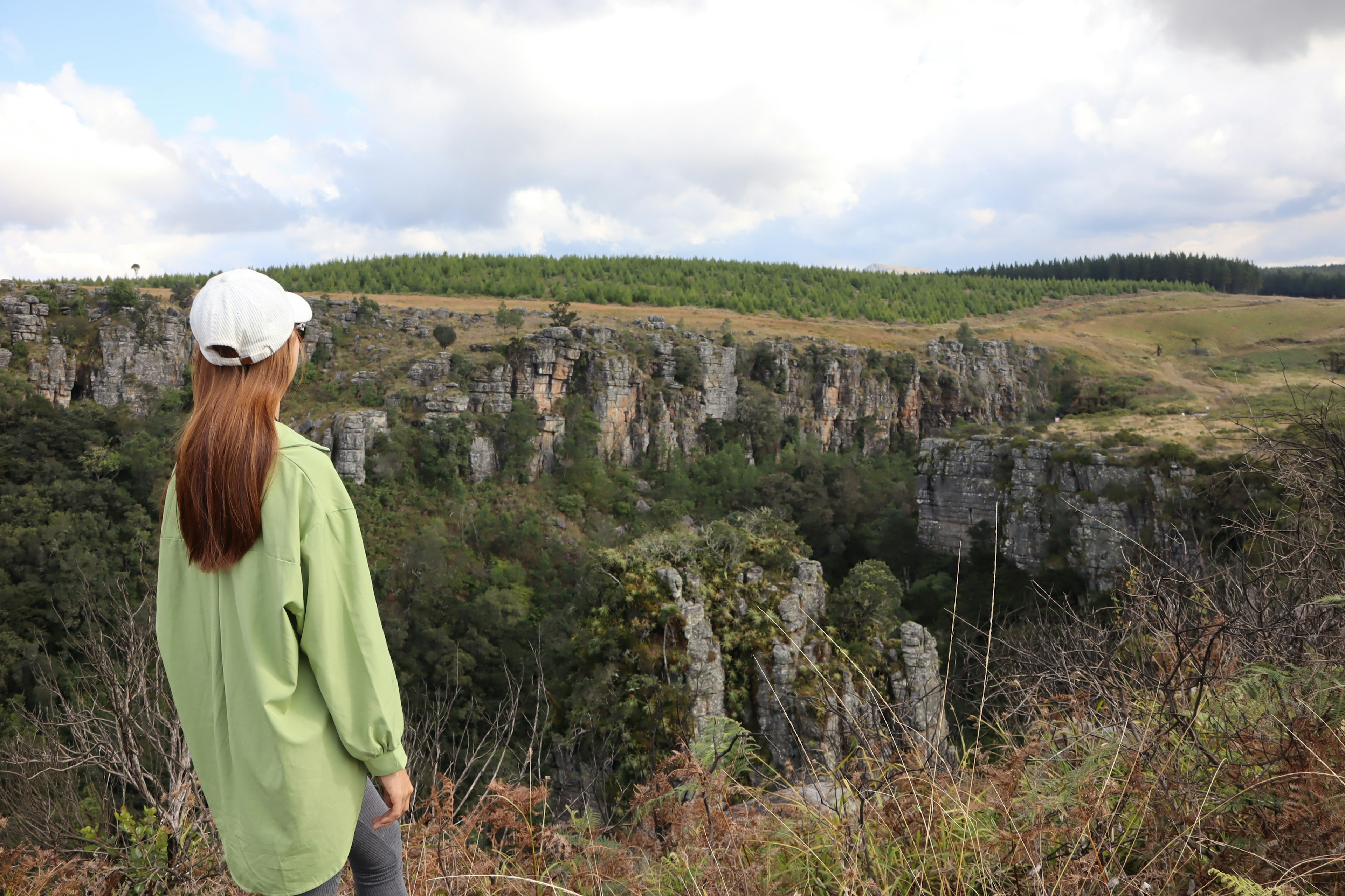 女性が緑のシャツを着て崖を見つめている風景